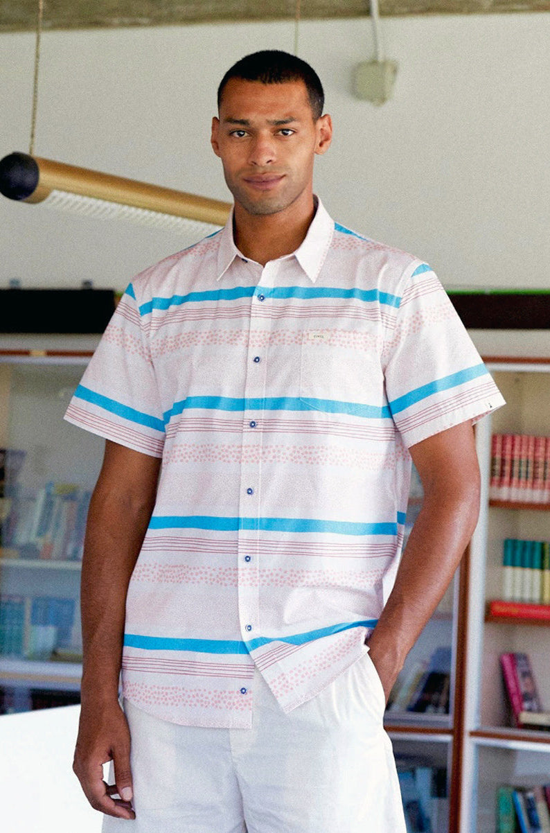 Male model wearing coral and blue striped button down shirt with white pants in library