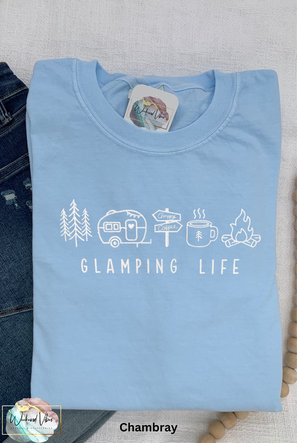 Embroidered Glamping Life comfort colors tee with camping icons. Icons include: A tree, travel trailer, camping signs, coffee cup, and campfire. Embroidery is done in white thread on a blue Comfort Colors t-shirt.