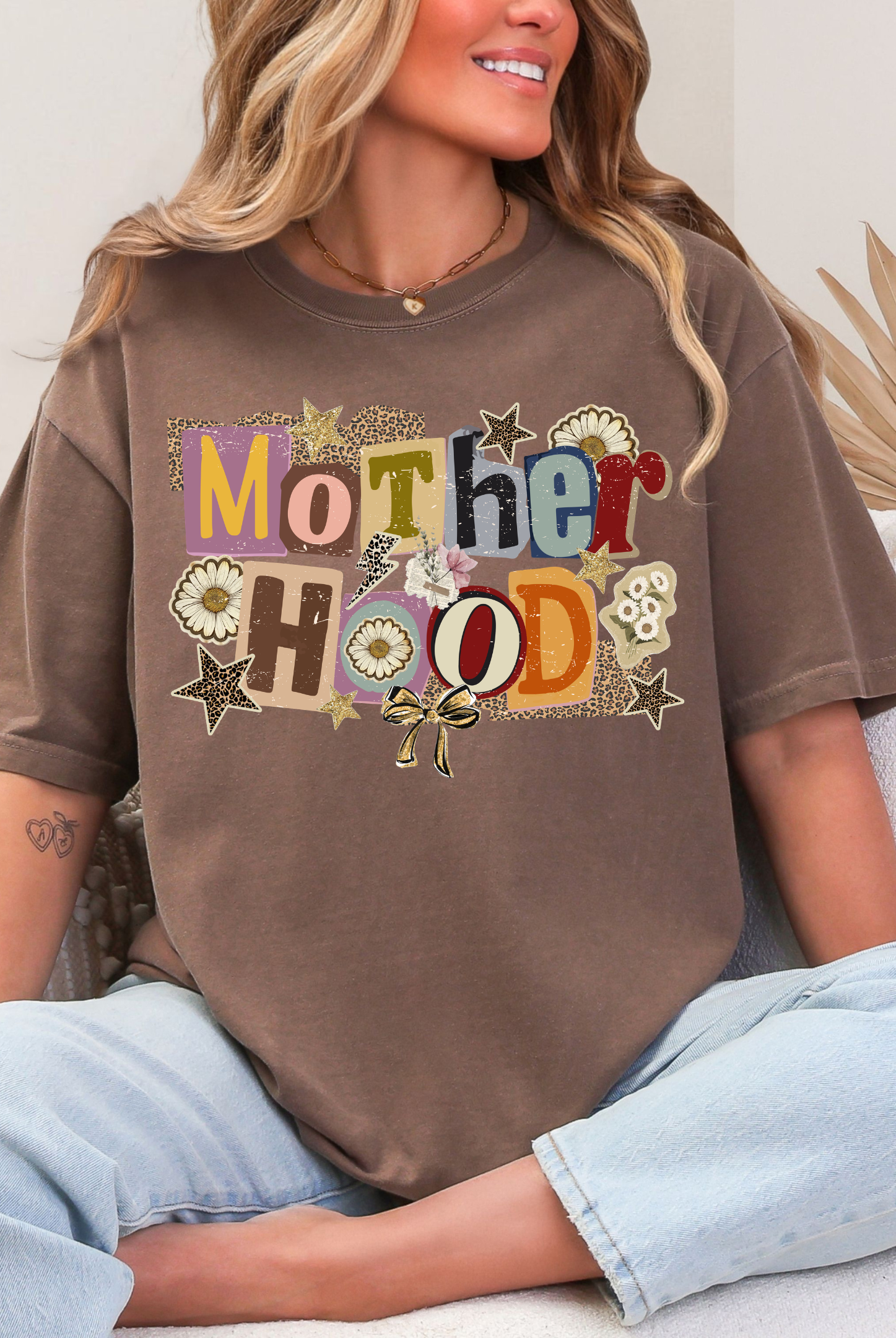 Woman wearing a brown t-shirt with 'Mother Hood' printed on it, sitting on a couch.