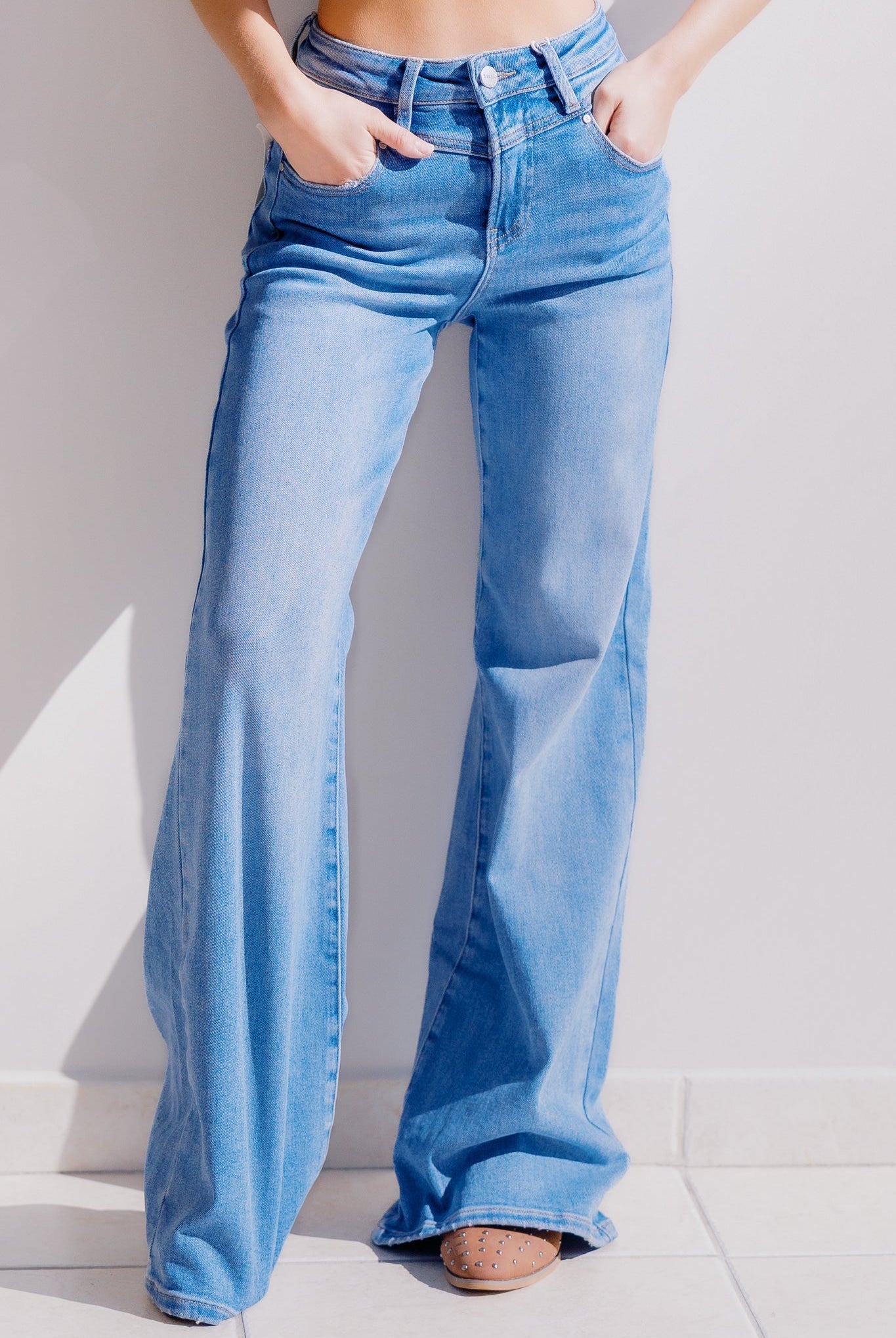 Woman wearing light blue flared jeans against a white background