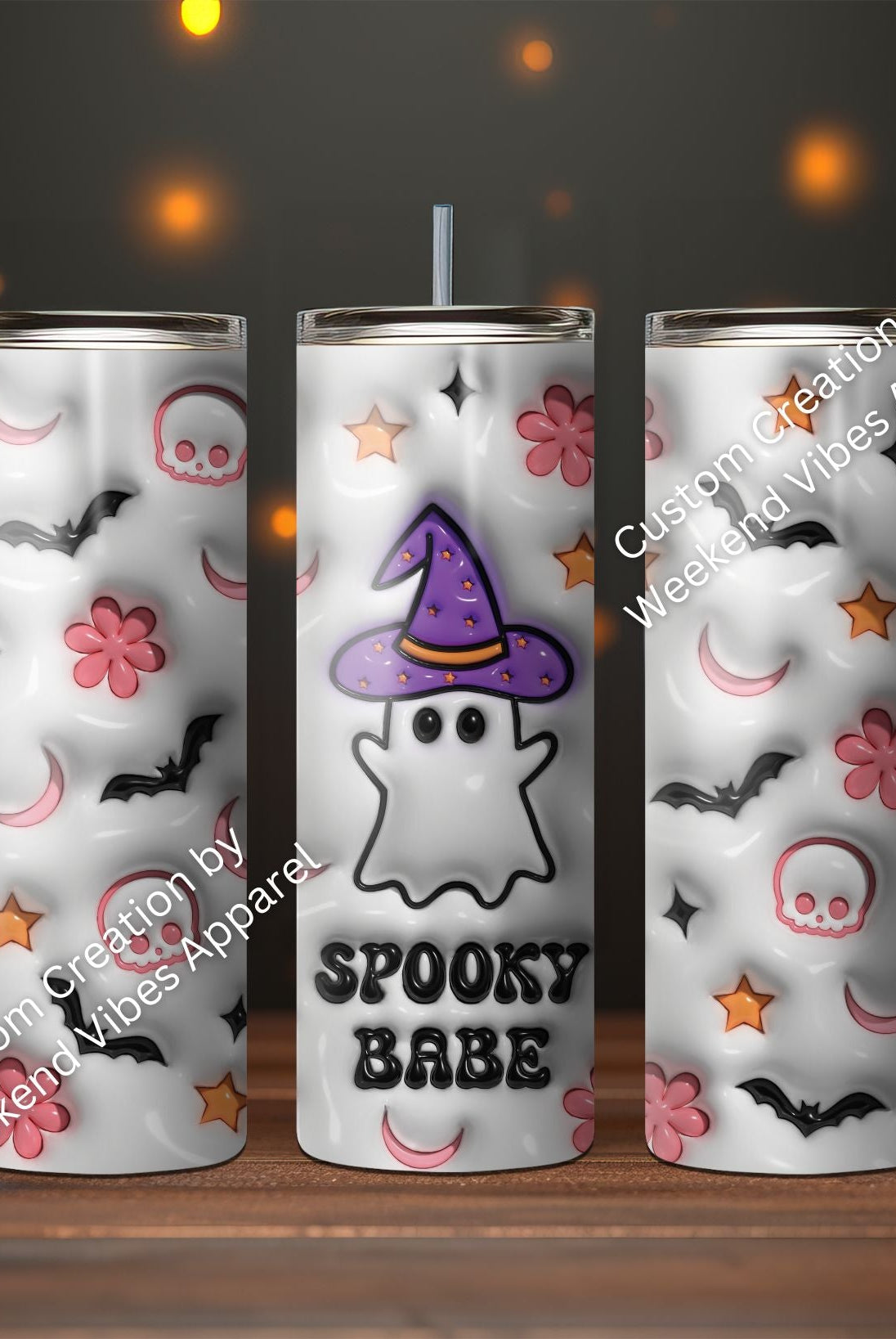 A set of three Spooky Babe Ghost Tumblers with Halloween-themed designs, including elements like bats, moons, and skulls, displayed in front of pumpkin lights.