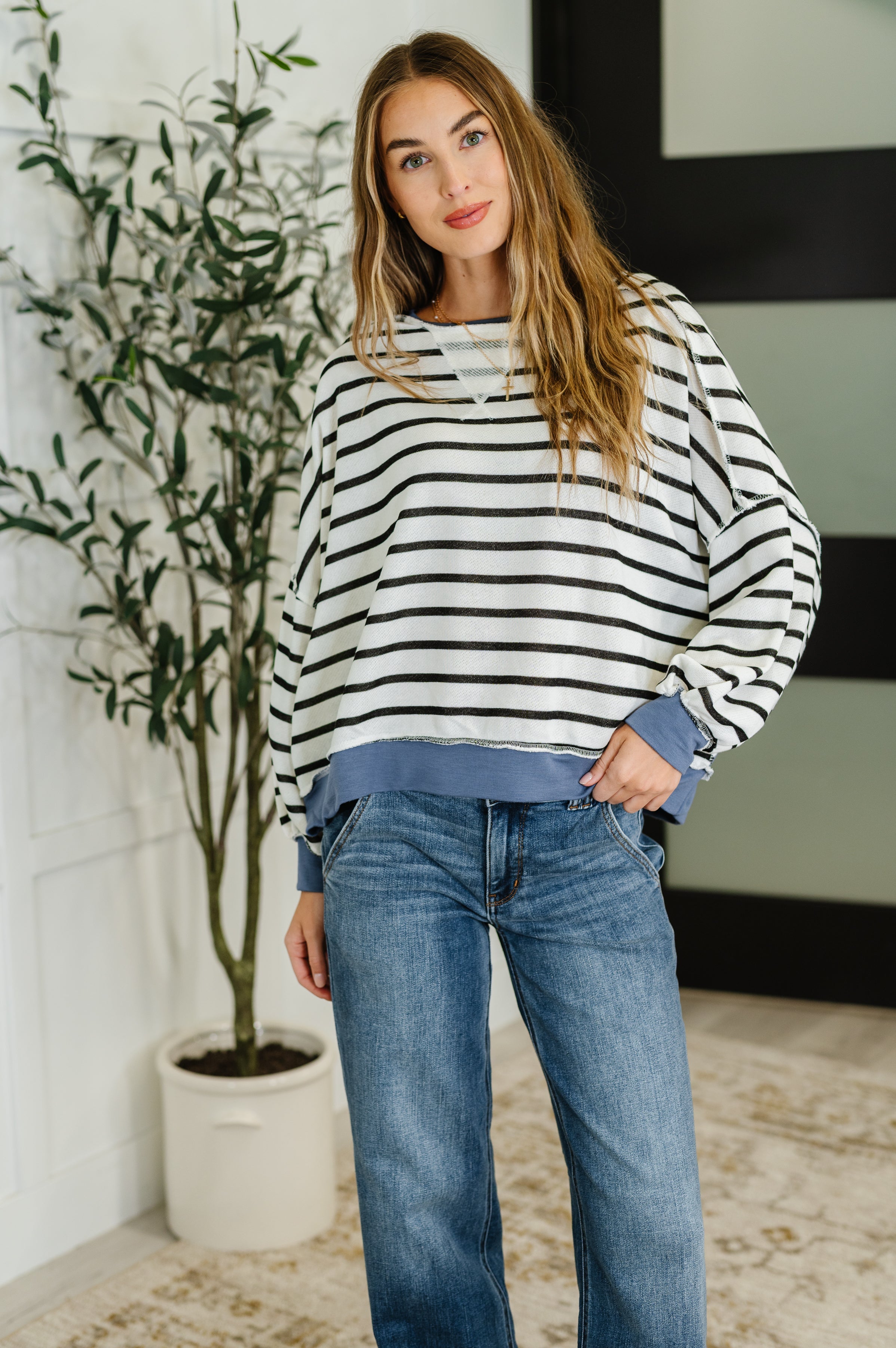 Woman wearing a striped sweater and jeans standing indoors with a plant in the background