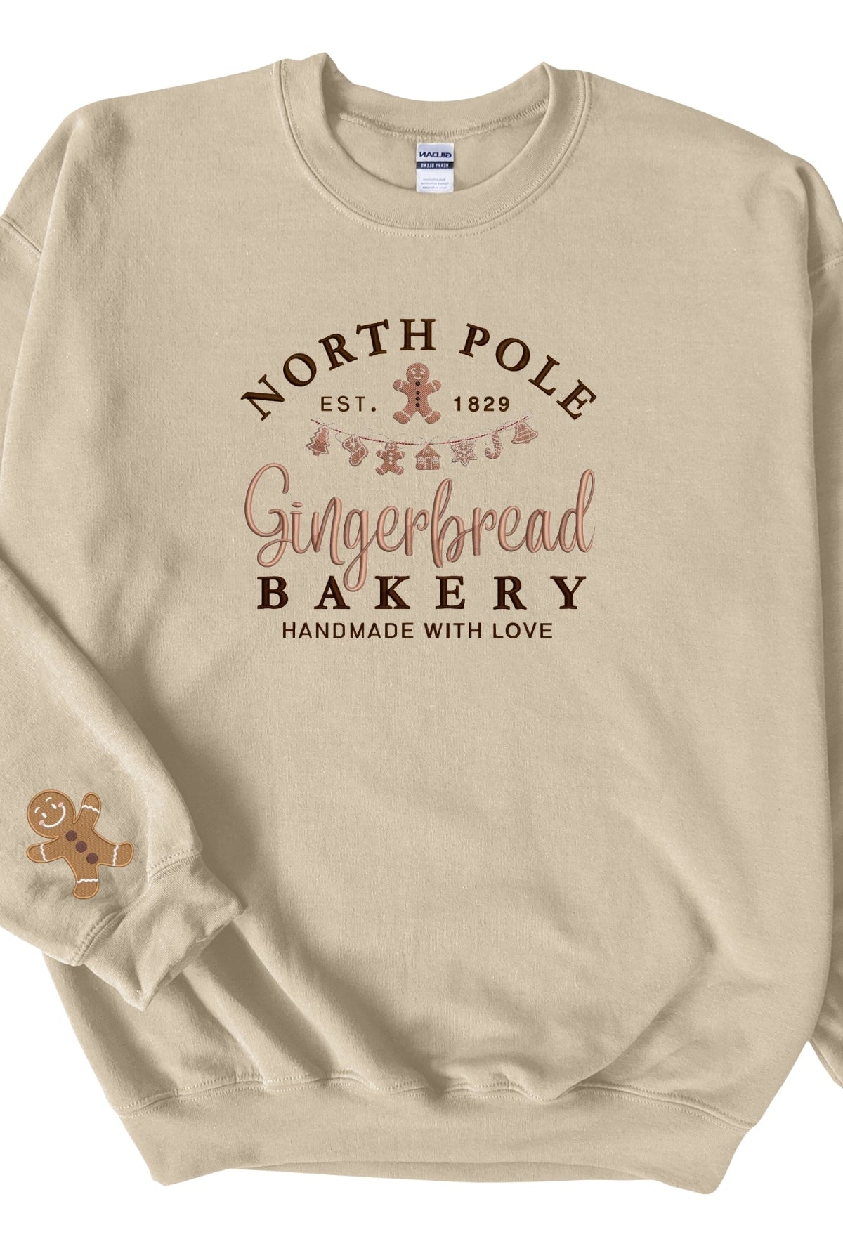 A beige sweatshirt with 'North Pole Gingerbread Bakery' embroidered on the chest and a small embroidered gingerbread man on the right sleeve.