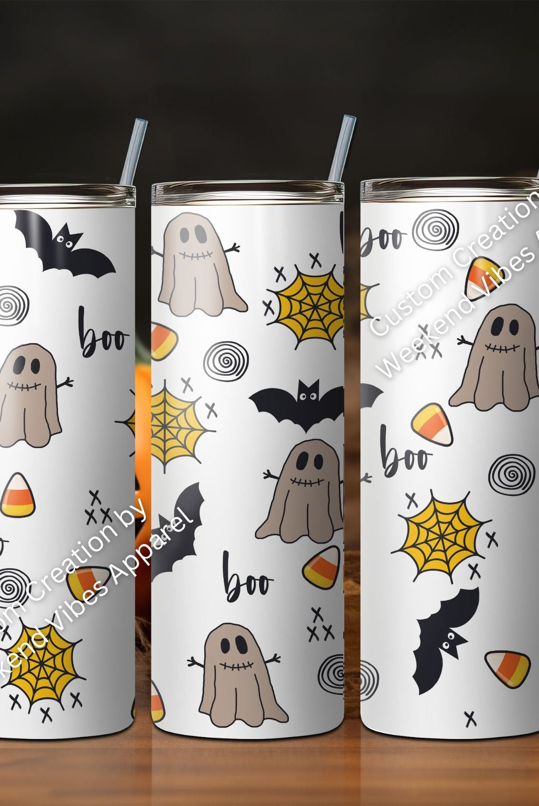 A set of three skinny tumblers with Halloween-themed designs, including ghosts and candy corn, displayed with pumpkins in the background.