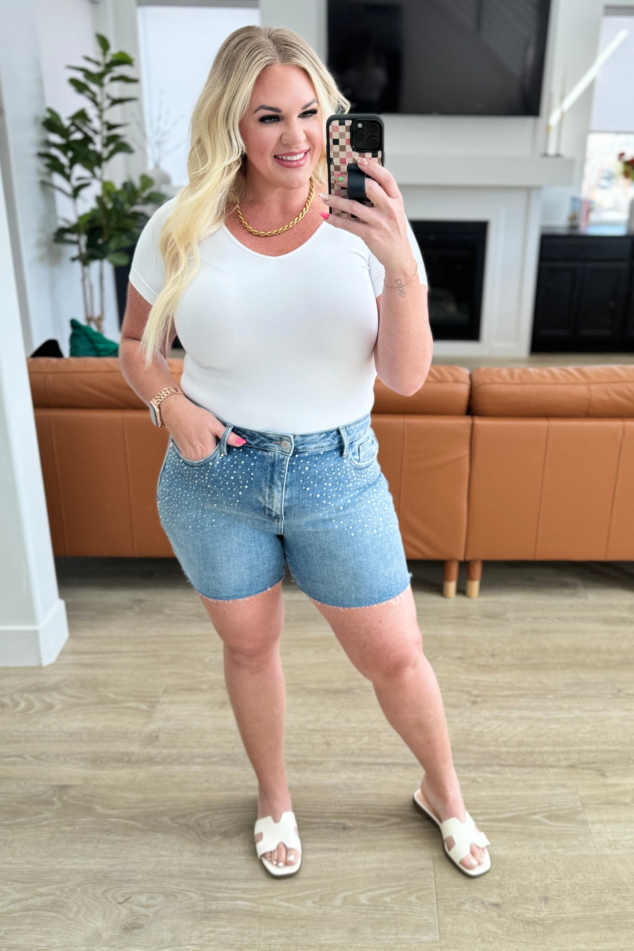 Kirra taking a selfie in a living room wearing a white top and denim shorts.