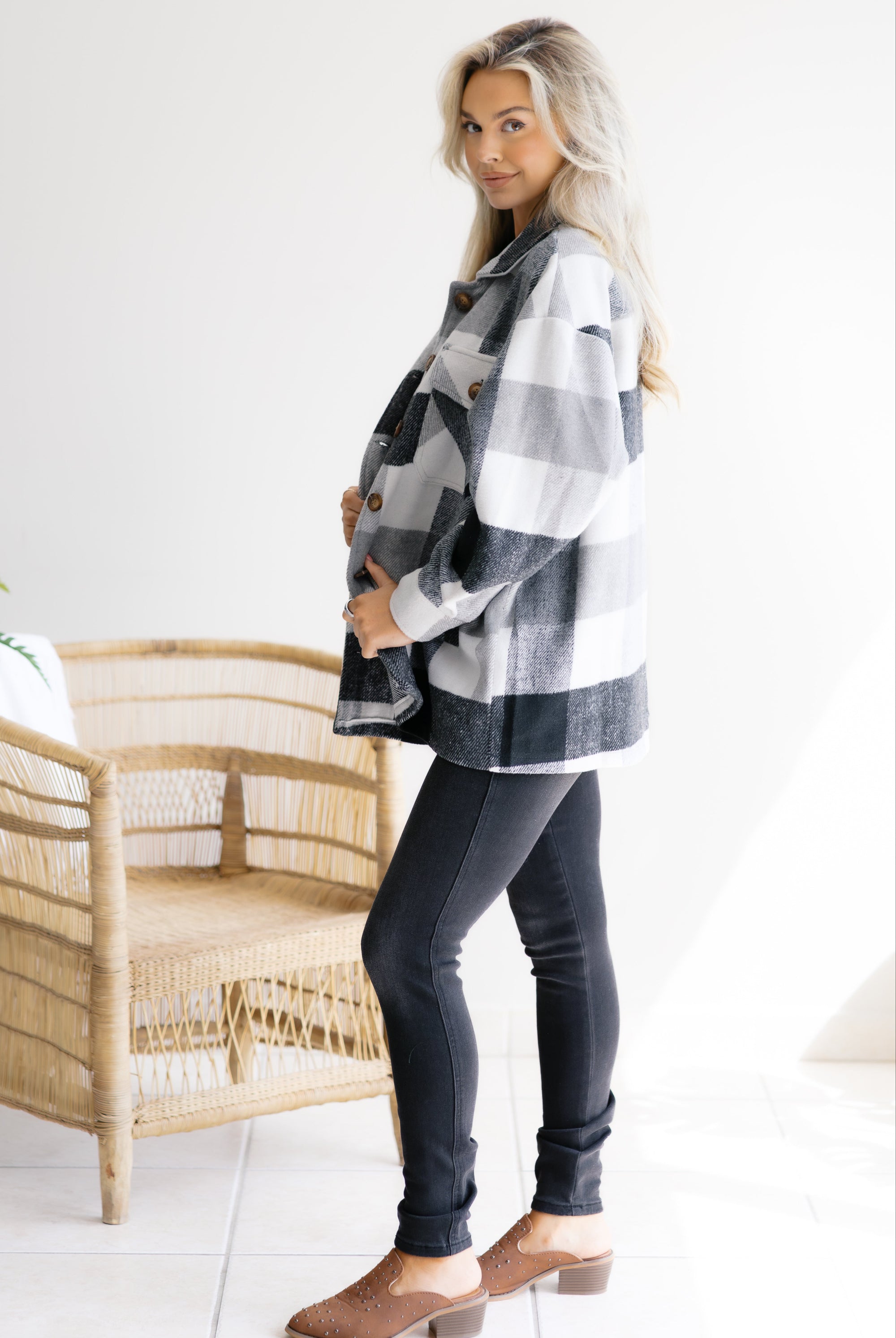 Woman wearing a plaid shirt and dark jeans standing in a room with a wicker chair.