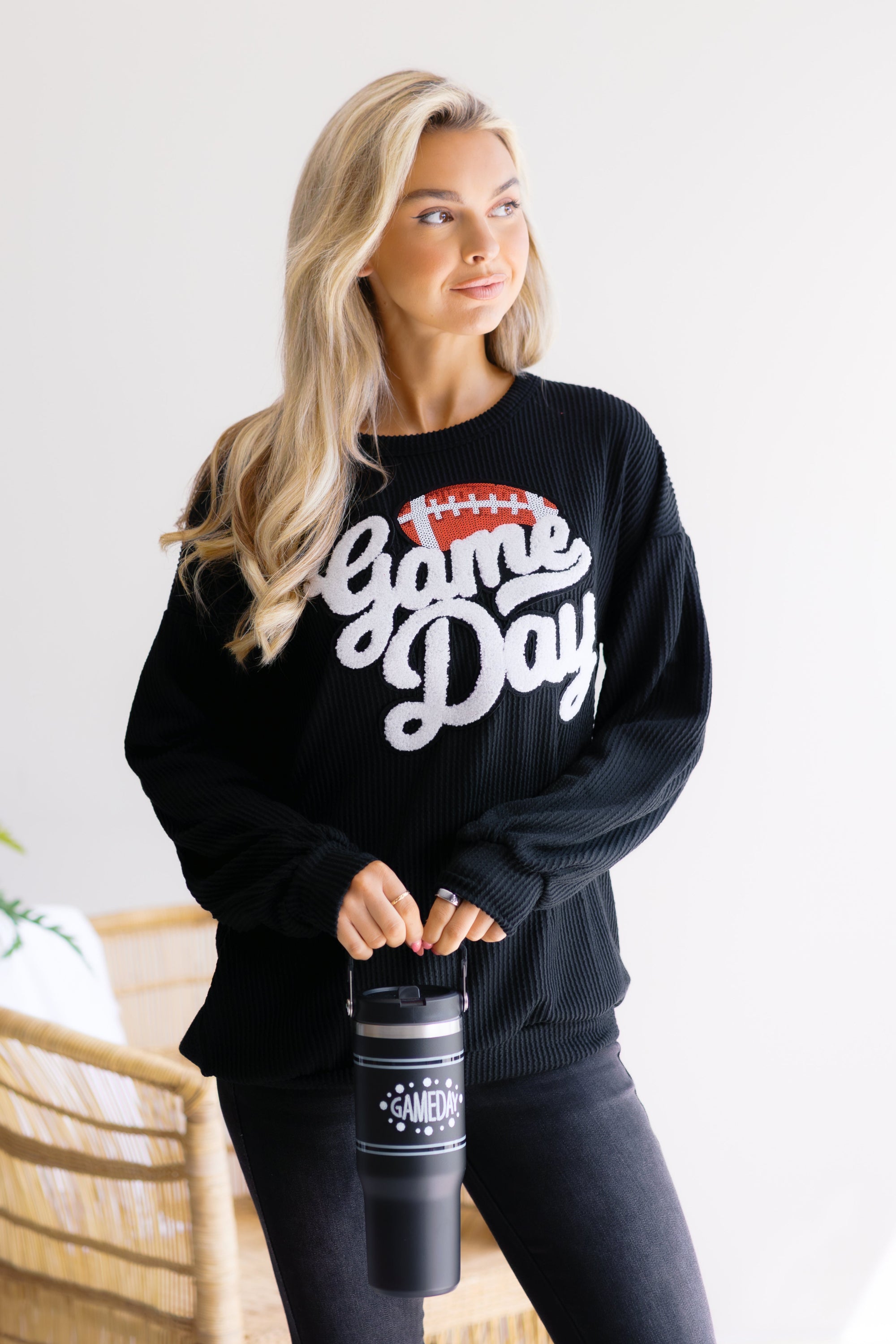 Woman wearing a black 'Game Day' sweatshirt holding a black tumbler.