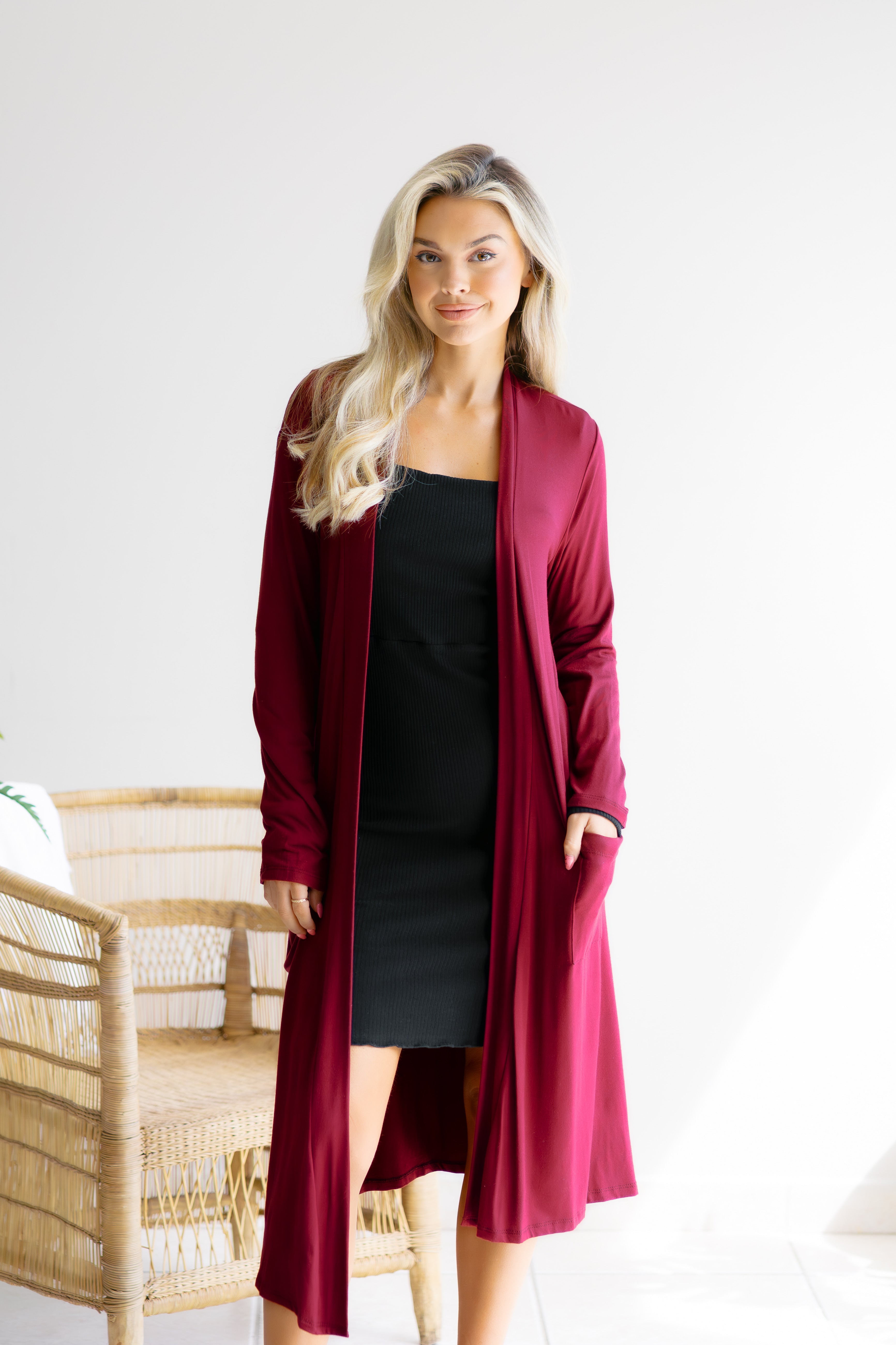 Woman wearing a burgundy cardigan over a black dress on a white background