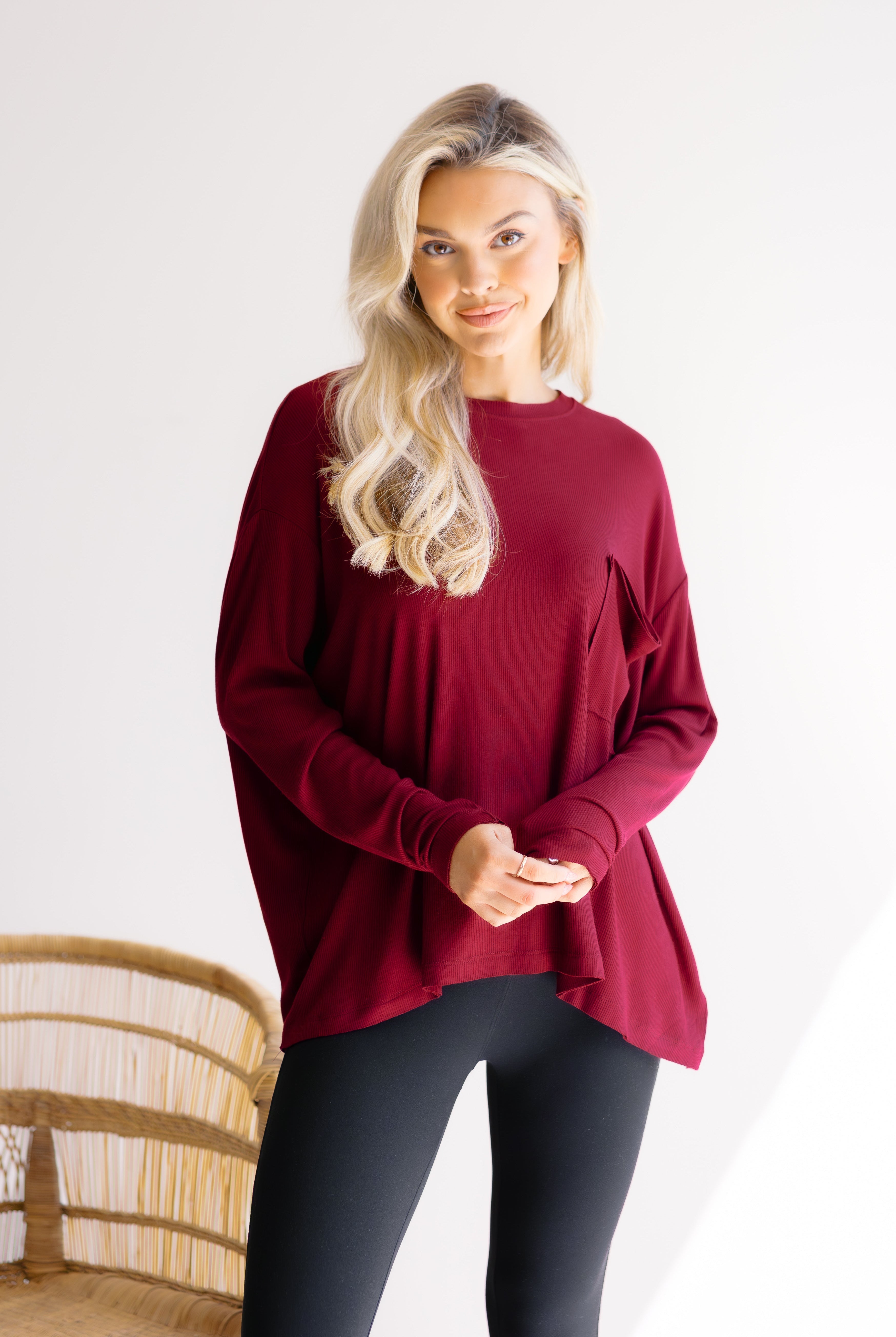 Woman wearing a burgundy long-sleeve top and black leggings on a white background