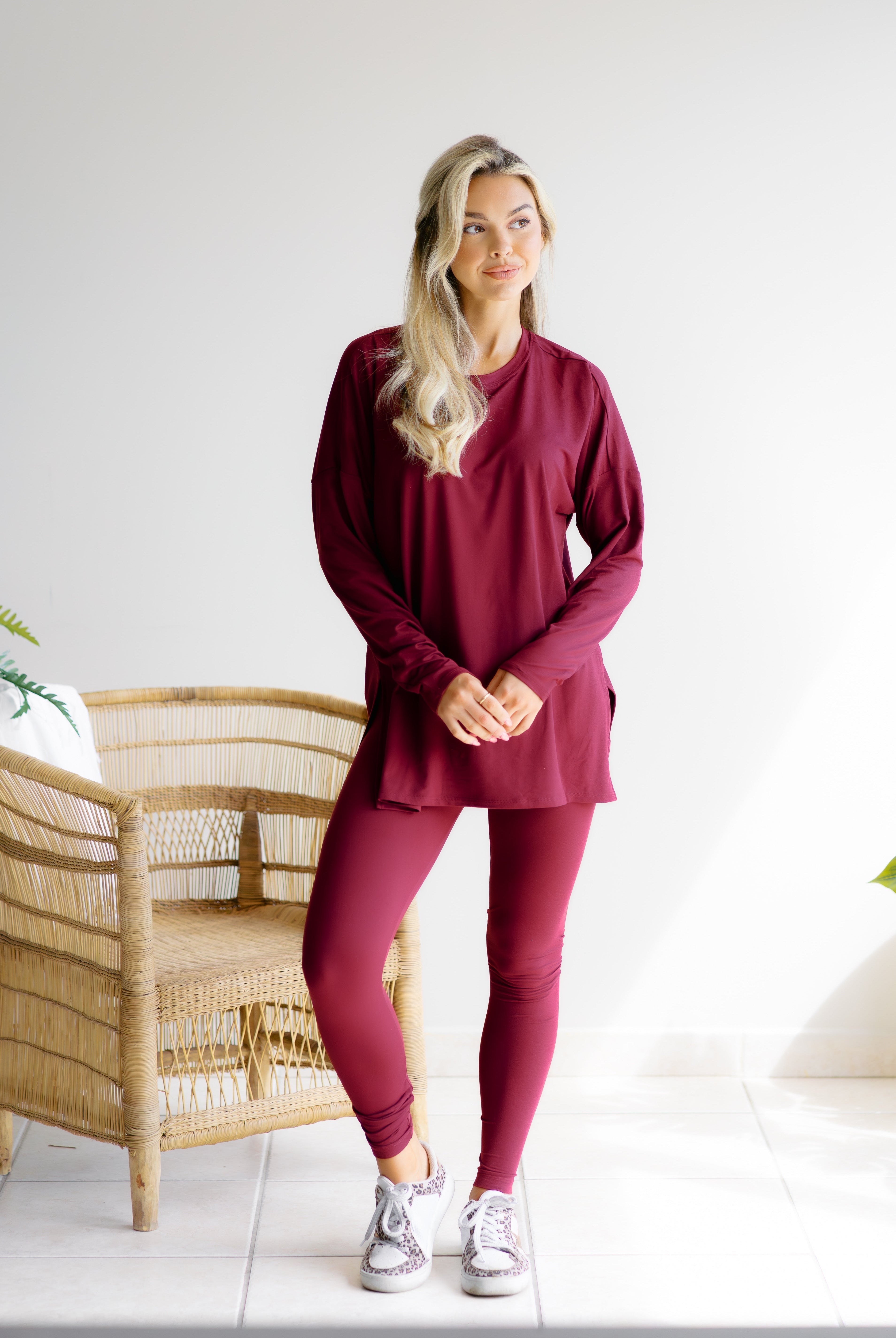 Woman wearing a crimson lounge outfit while standing in a room with a wicker chair.