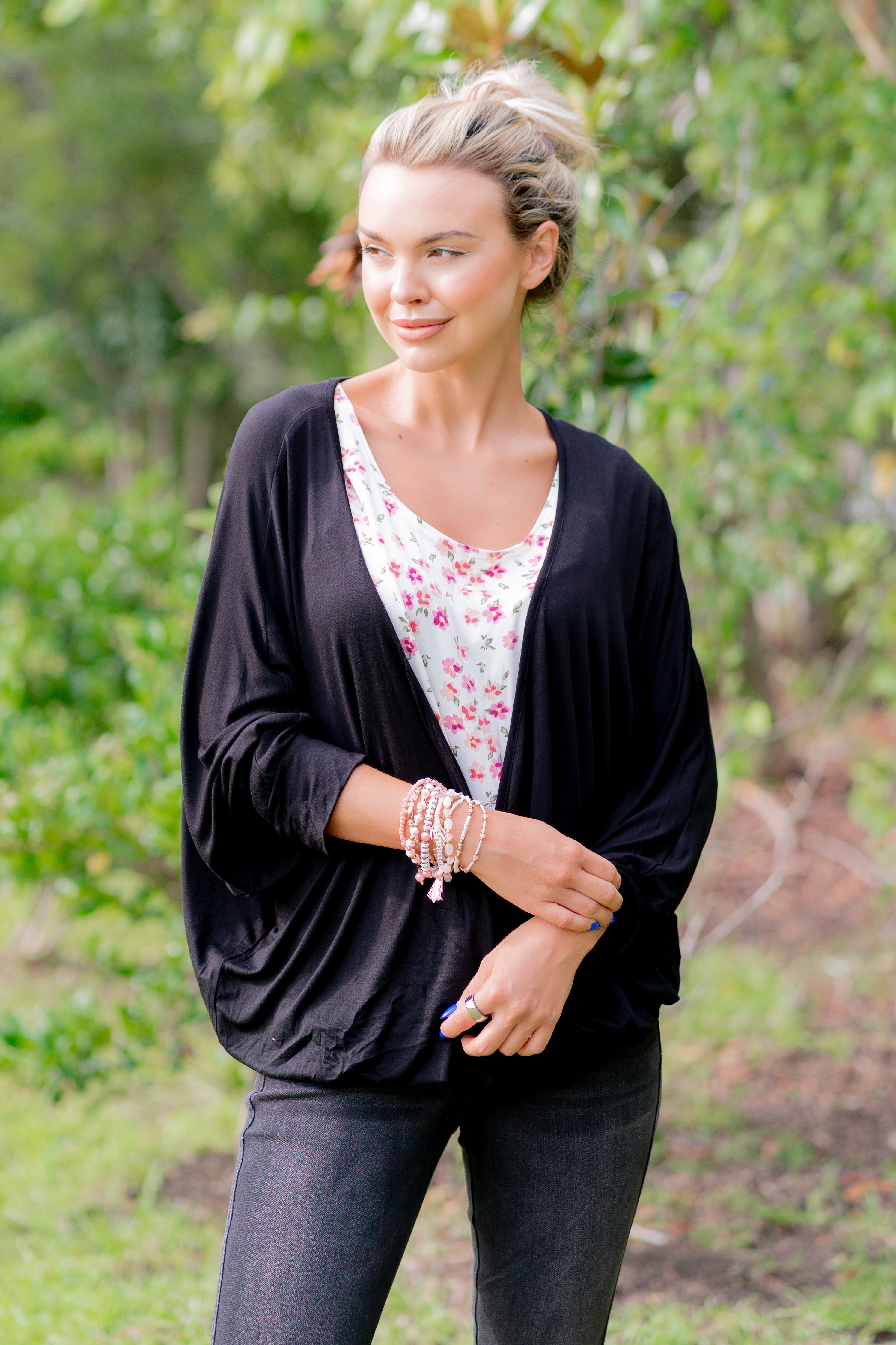 Woman wearing a black cardigan over a floral top with a natural background
