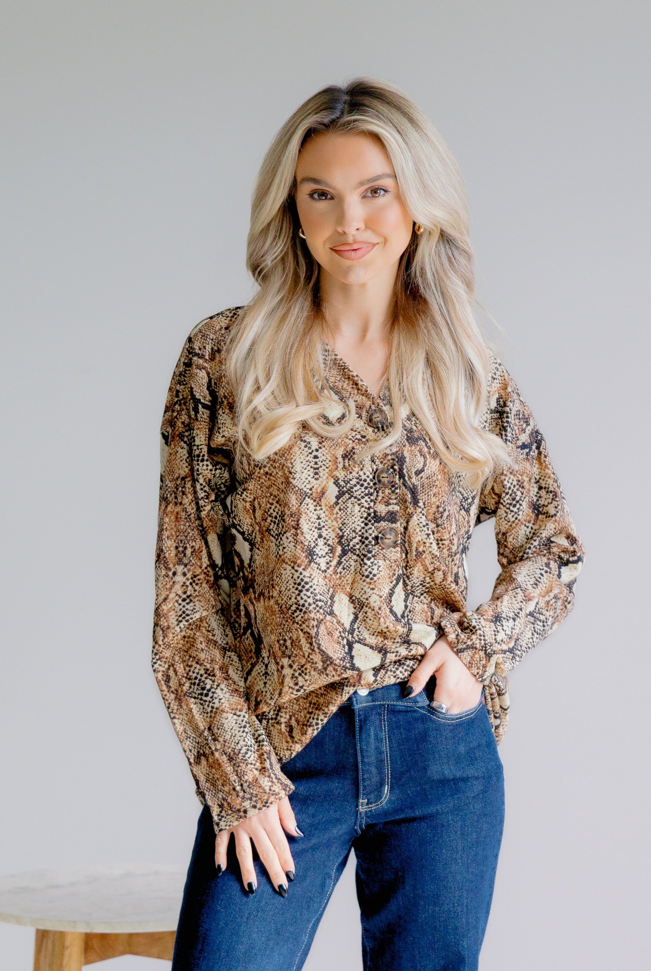 Woman wearing a patterned blouse and blue jeans against a plain background