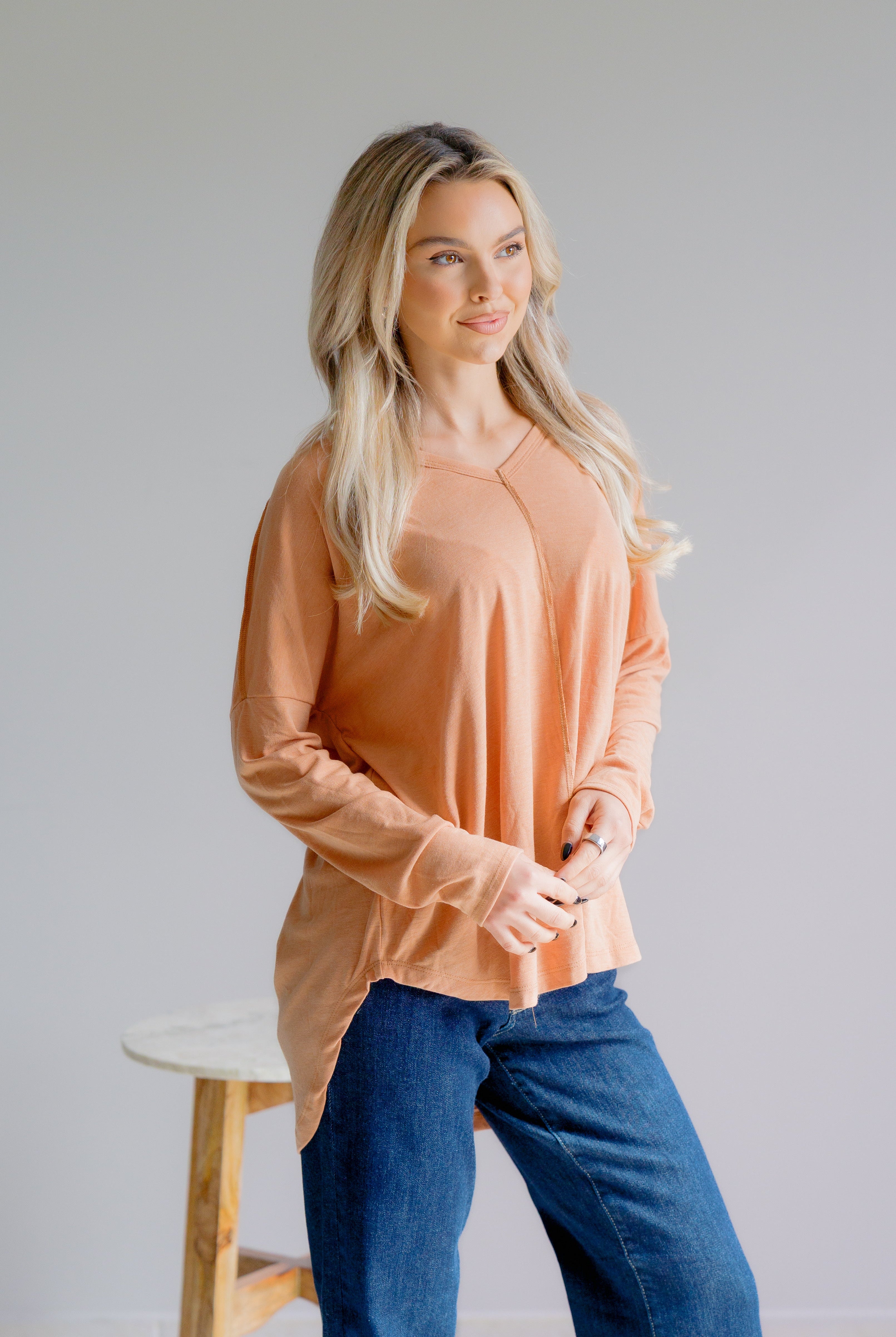 Woman wearing a peach long-sleeve top and blue jeans against a plain background