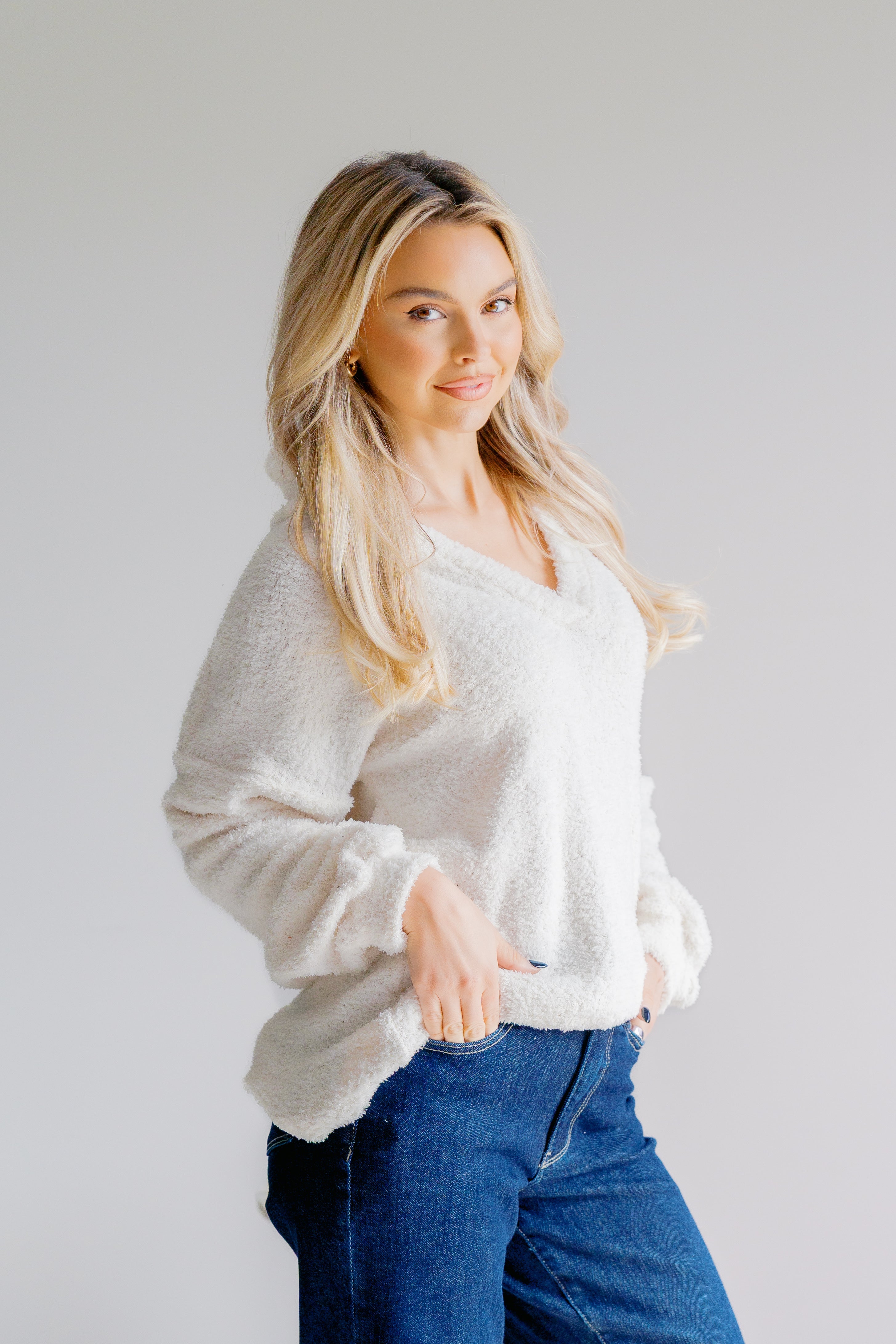 Woman wearing a white sweater and blue jeans against a plain background