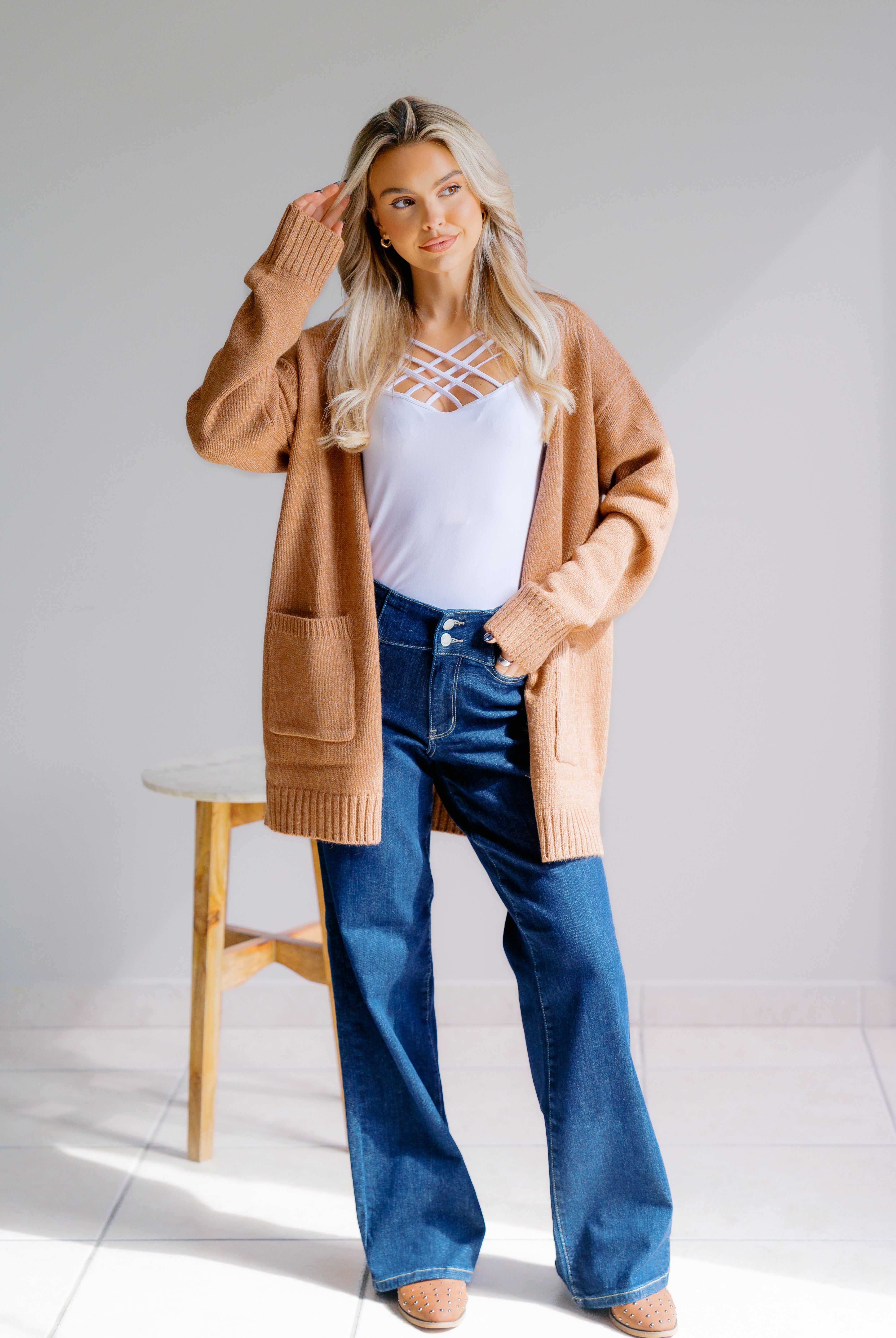 Woman wearing a beige cardigan, white top, and blue jeans in a minimalistic setting.