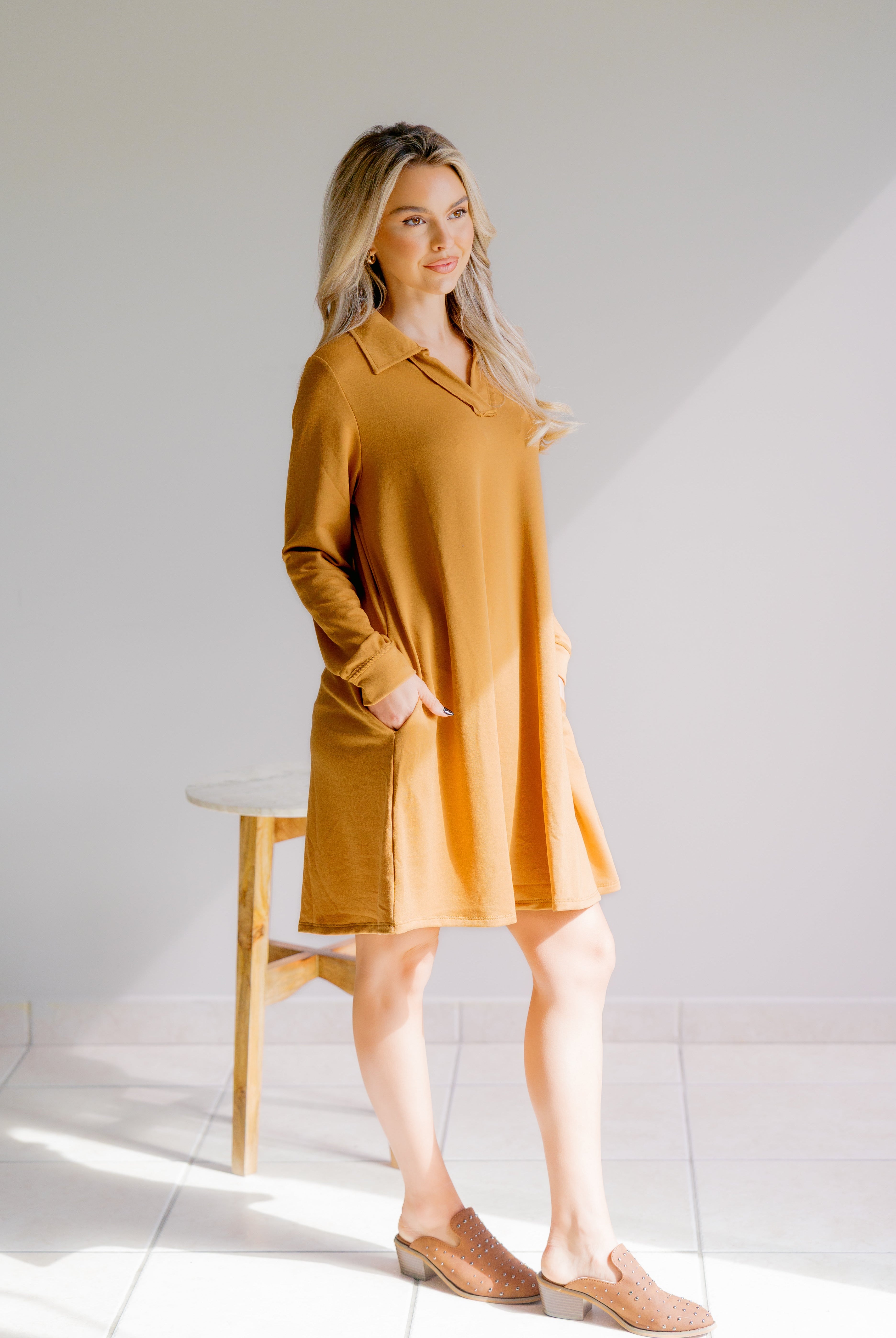 Woman wearing a mustard yellow dress standing against a white background