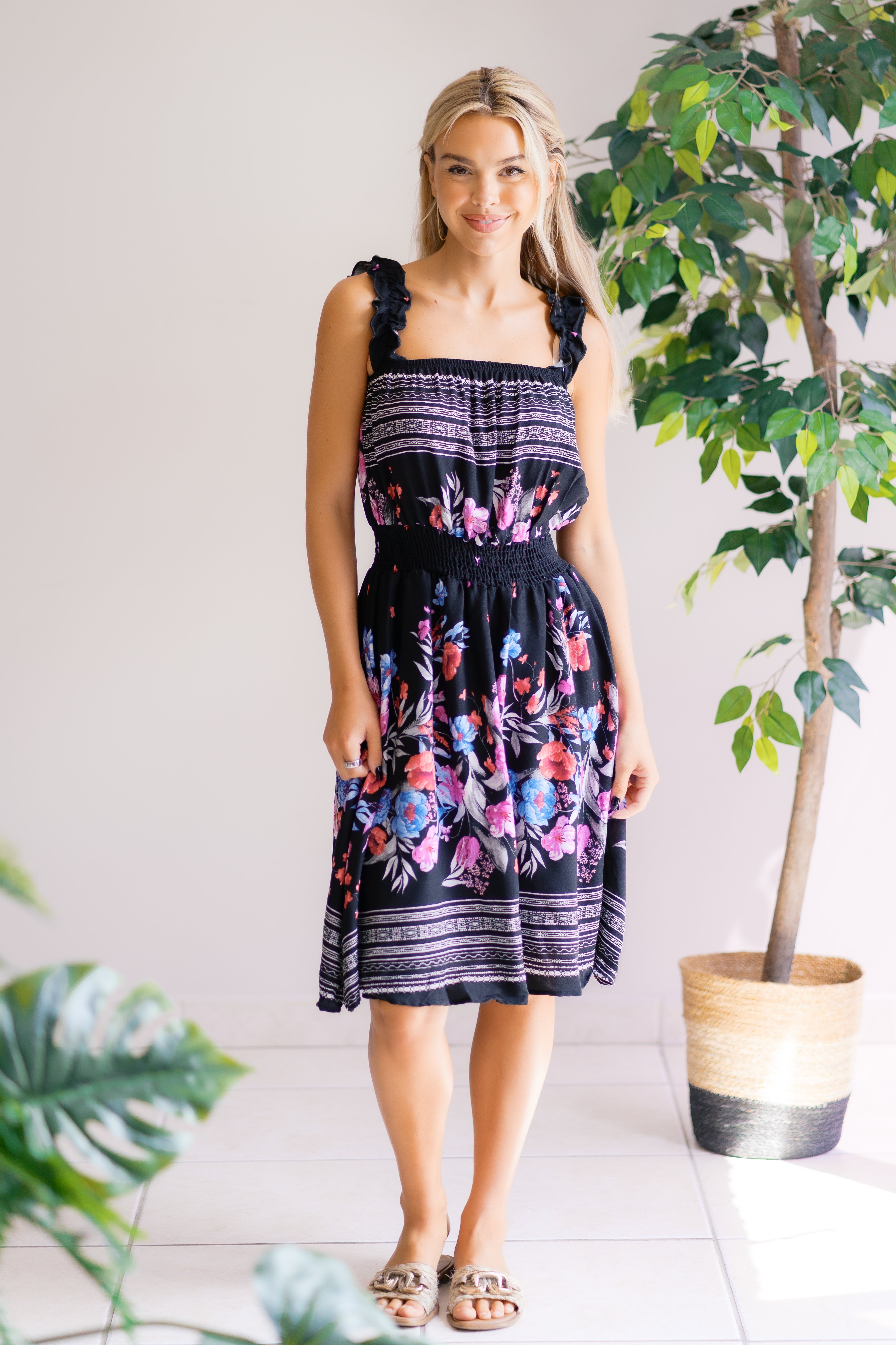 Woman wearing a floral dress standing indoors with plants around