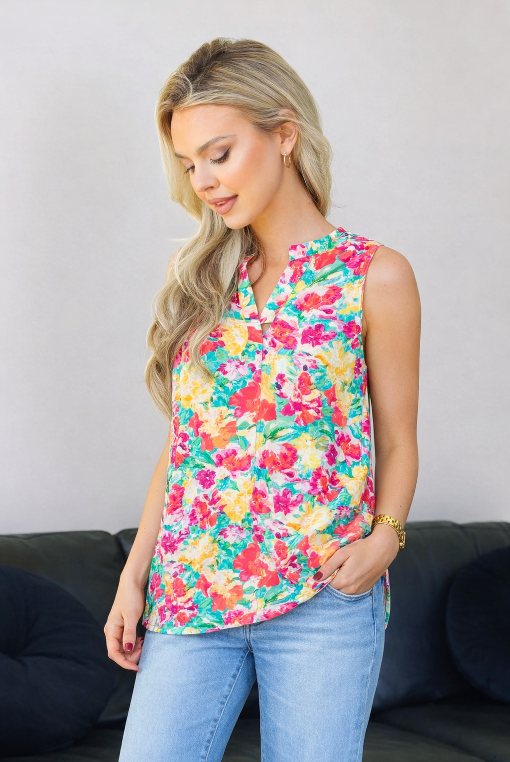 Woman wearing a colorful floral sleeveless top and blue jeans against a gray background.