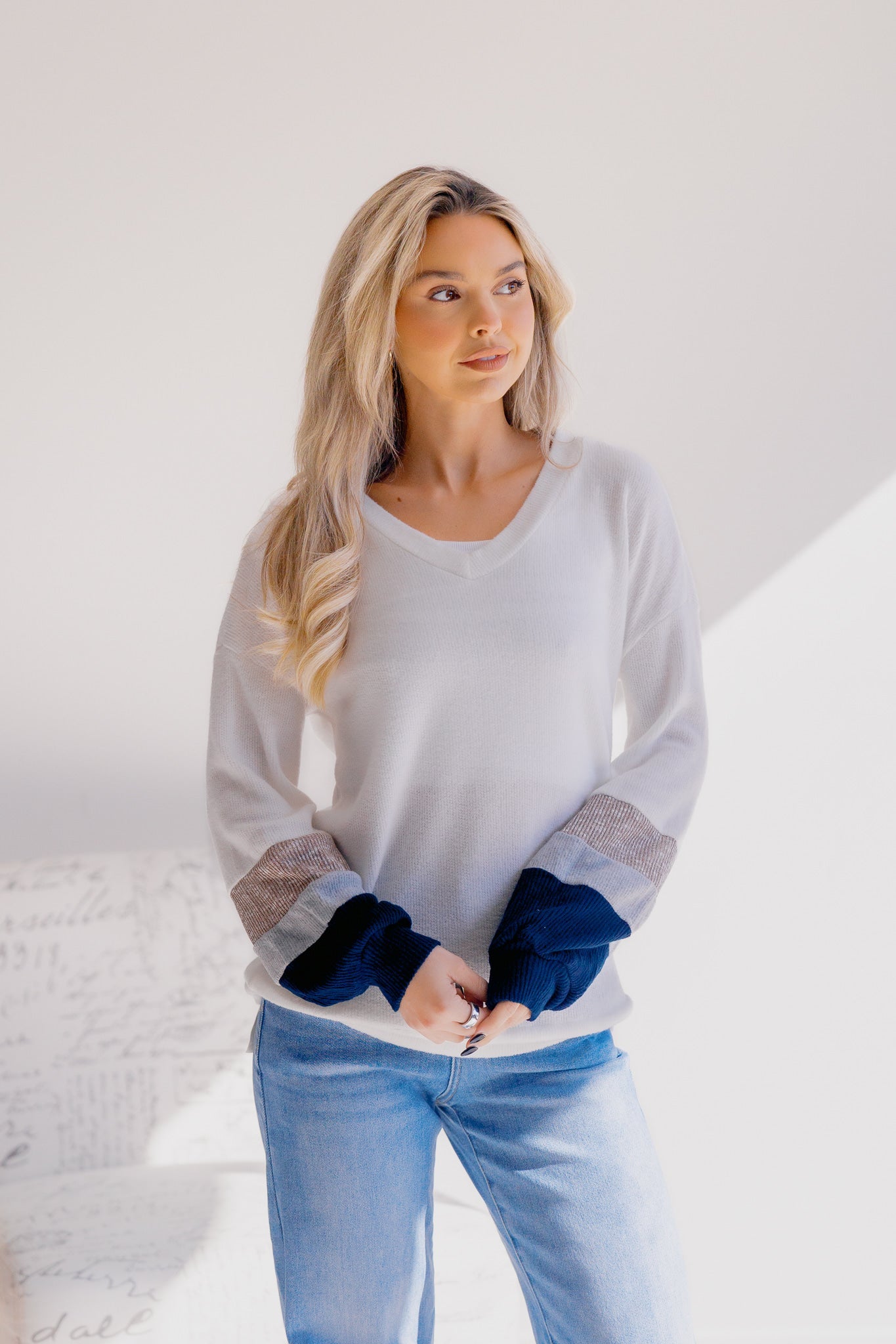 Woman wearing a white sweater with blue accents and light blue jeans on a white background