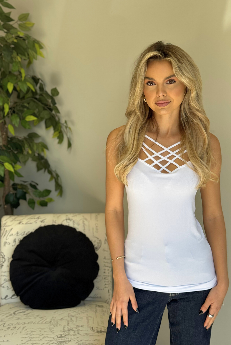 Woman wearing a white tank top with criss-cross design in a casual setting.