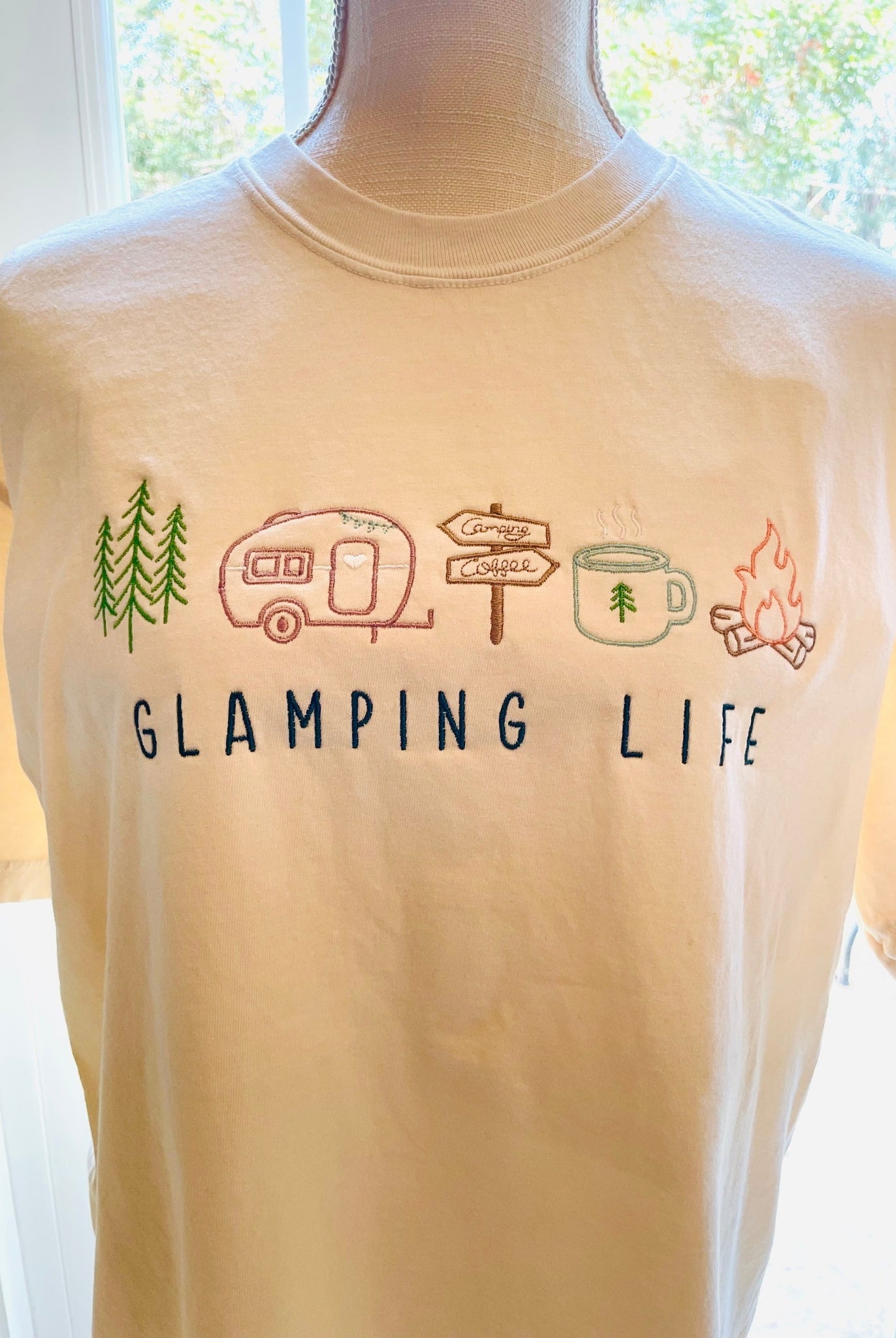 Embroidered natural Comfort Colors tee with embroidered "GLAMPING LIFE" and colorful camping icons. Icons include: A tree, travel trailer, camping signs, coffee cup, and campfire.