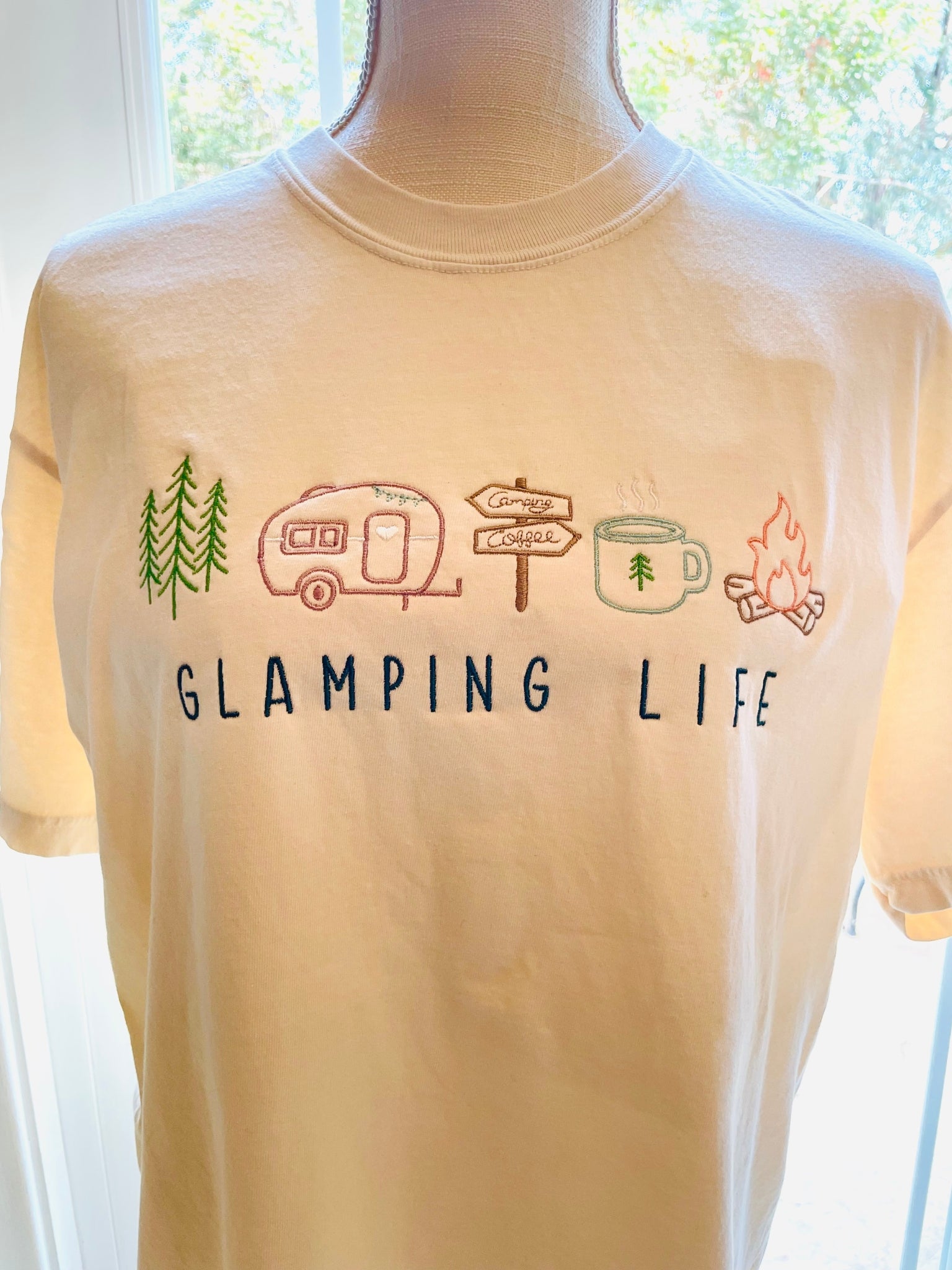 Embroidered natural Comfort Colors tee with embroidered "GLAMPING LIFE" and colorful camping icons. Icons include: A tree, travel trailer, camping signs, coffee cup, and campfire.