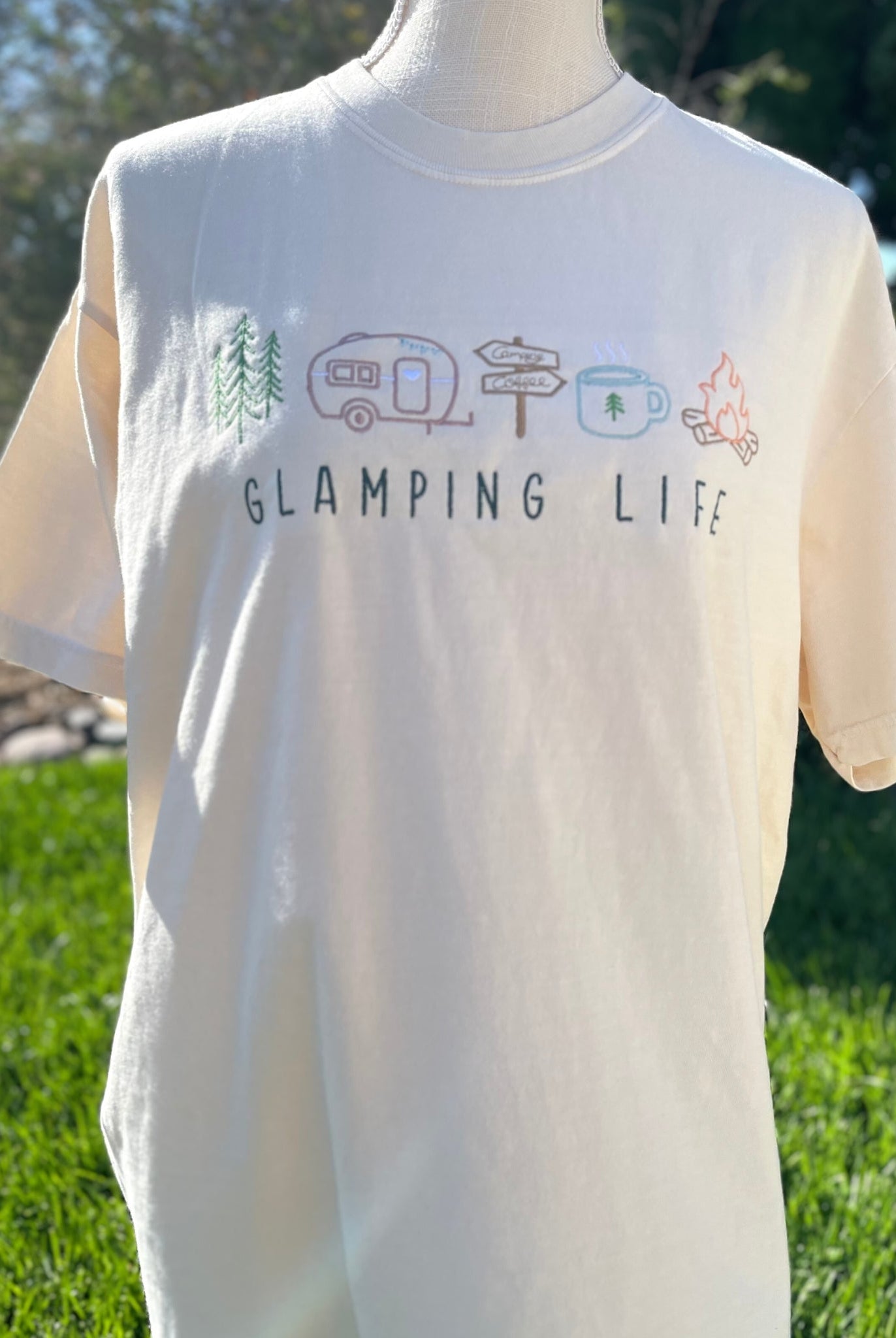 Embroidered Glamping Life tee with camping images. Images of trees, a travel trailer, signs, coffee mug, and campfire are embroidered above the words "GLAMPING LIFE" on a comfort colors t-shirt.