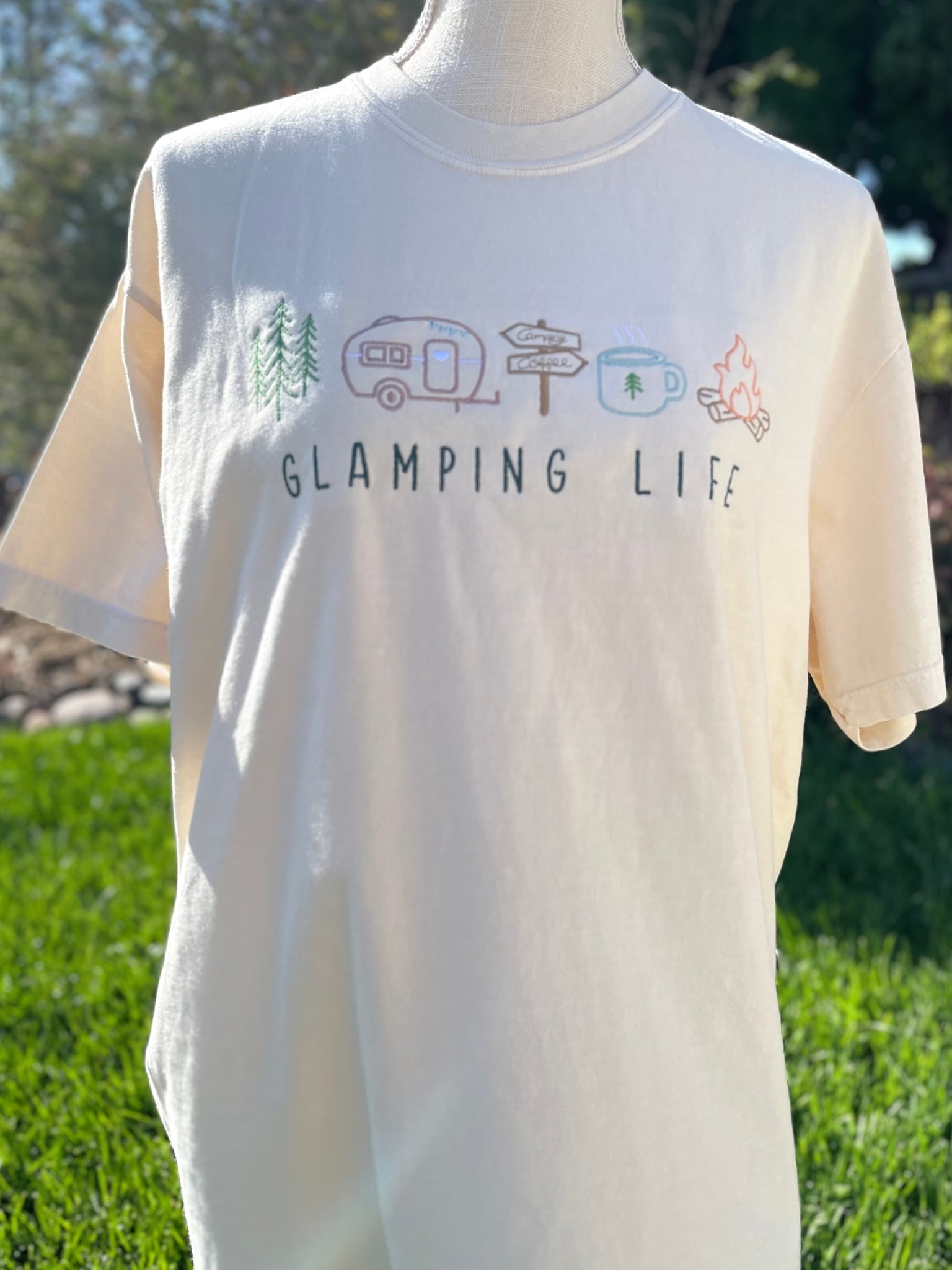 Embroidered Glamping Life tee with camping images. Images of trees, a travel trailer, signs, coffee mug, and campfire are embroidered above the words "GLAMPING LIFE" on a comfort colors t-shirt.