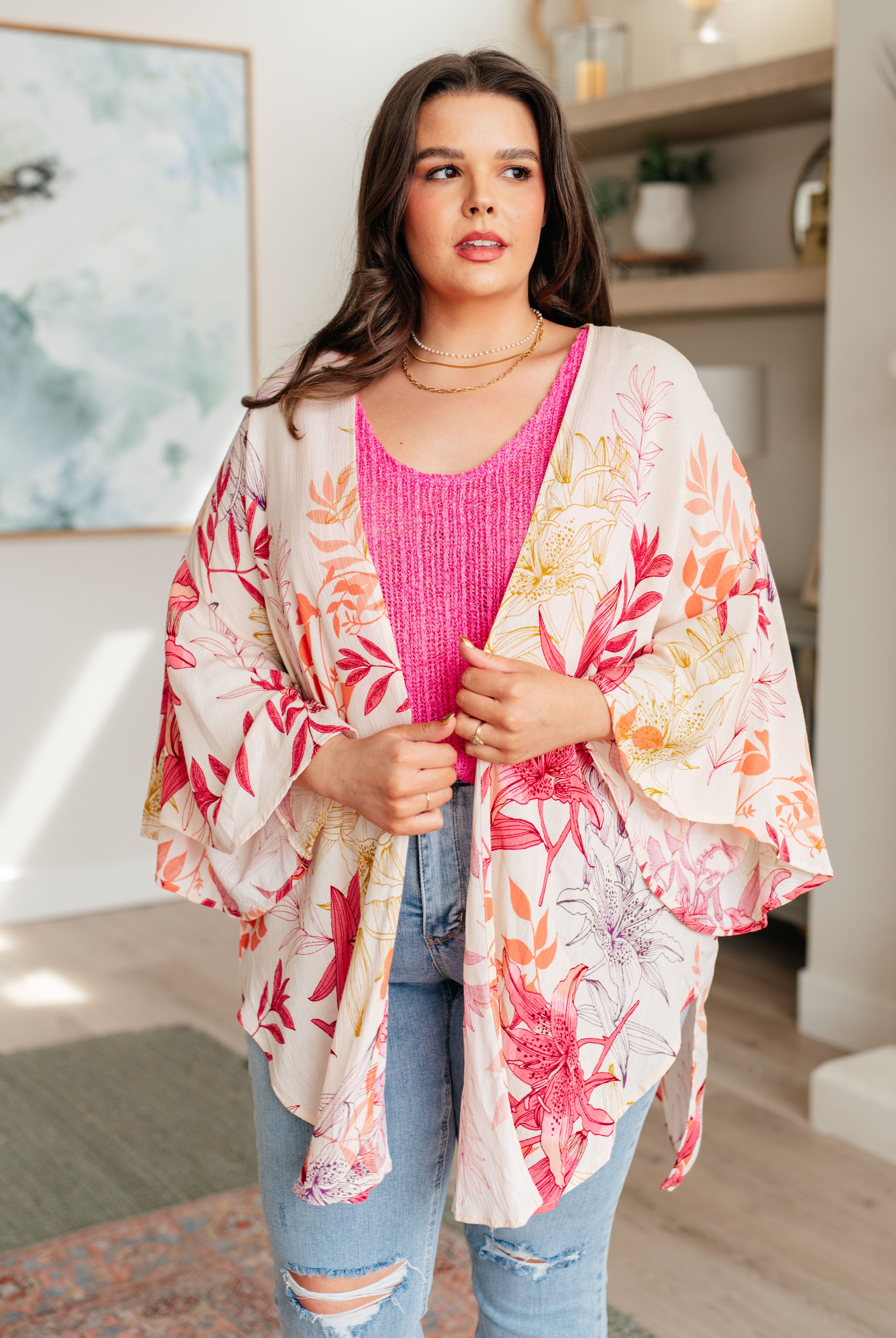 Woman wearing a floral kimono over a pink top and jeans in a room with decor.