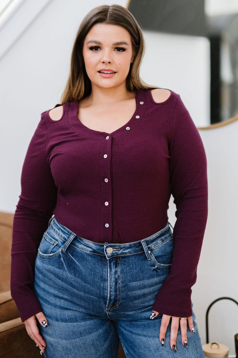 Brunette female model wearing plum-colored bodysuit and medium wash denim jeans