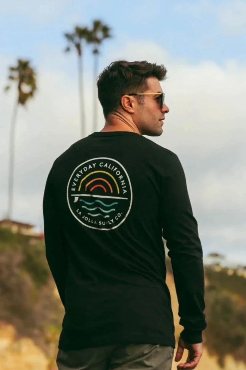 Male model with black long sleeved graphic t-shirt admiring cliff view at beach.