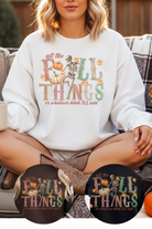 Person wearing a white sweatshirt with Halloween-themed text and graphics, sitting on a couch.