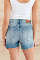 Backside photo of model Sabrina wearing Judy Blue cutoff shorts with a white tank top.