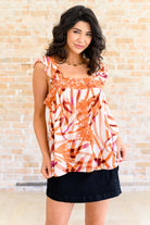 Woman wearing an orange and white patterned top with a black skirt against a beige brick wall.