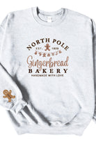 An ash gray sweatshirt with 'North Pole Gingerbread Bakery' embroidered on the chest and a small embroidered gingerbread man on the right sleeve.