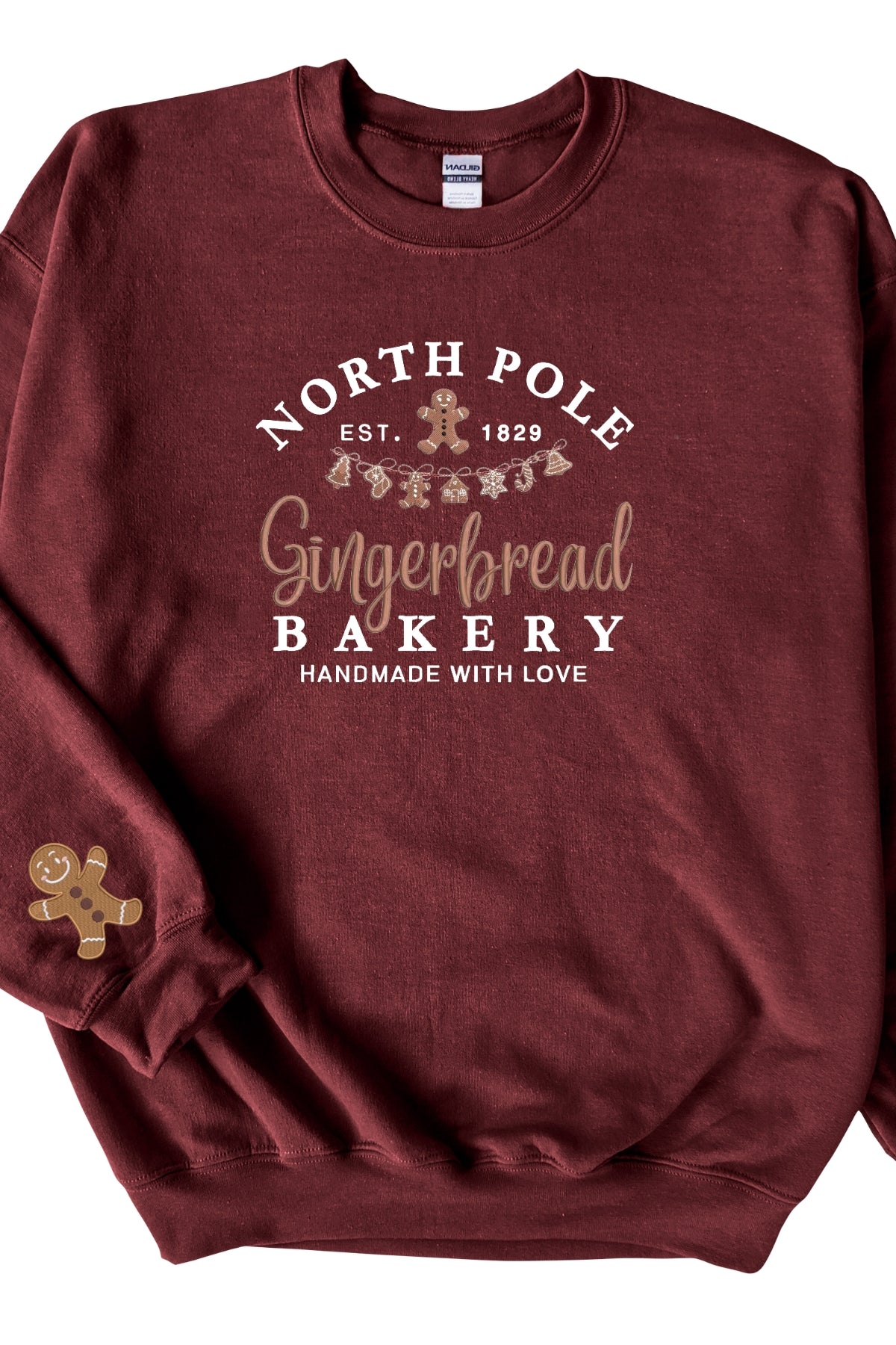 A cardinal red sweatshirt with 'North Pole Gingerbread Bakery' embroidered on the chest and a small embroidered gingerbread man on the right sleeve.