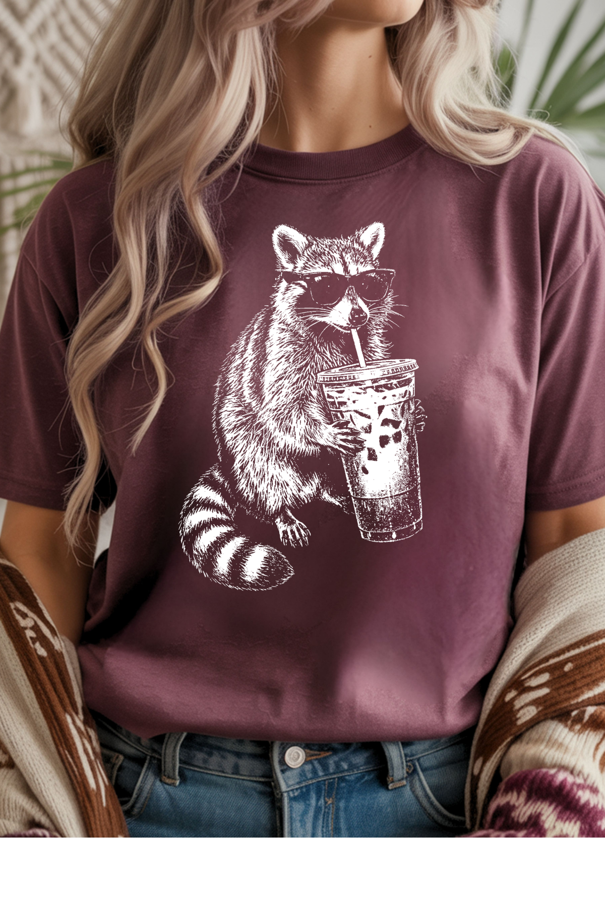 Person wearing a maroon t-shirt with a raccoon graphic holding a drink.