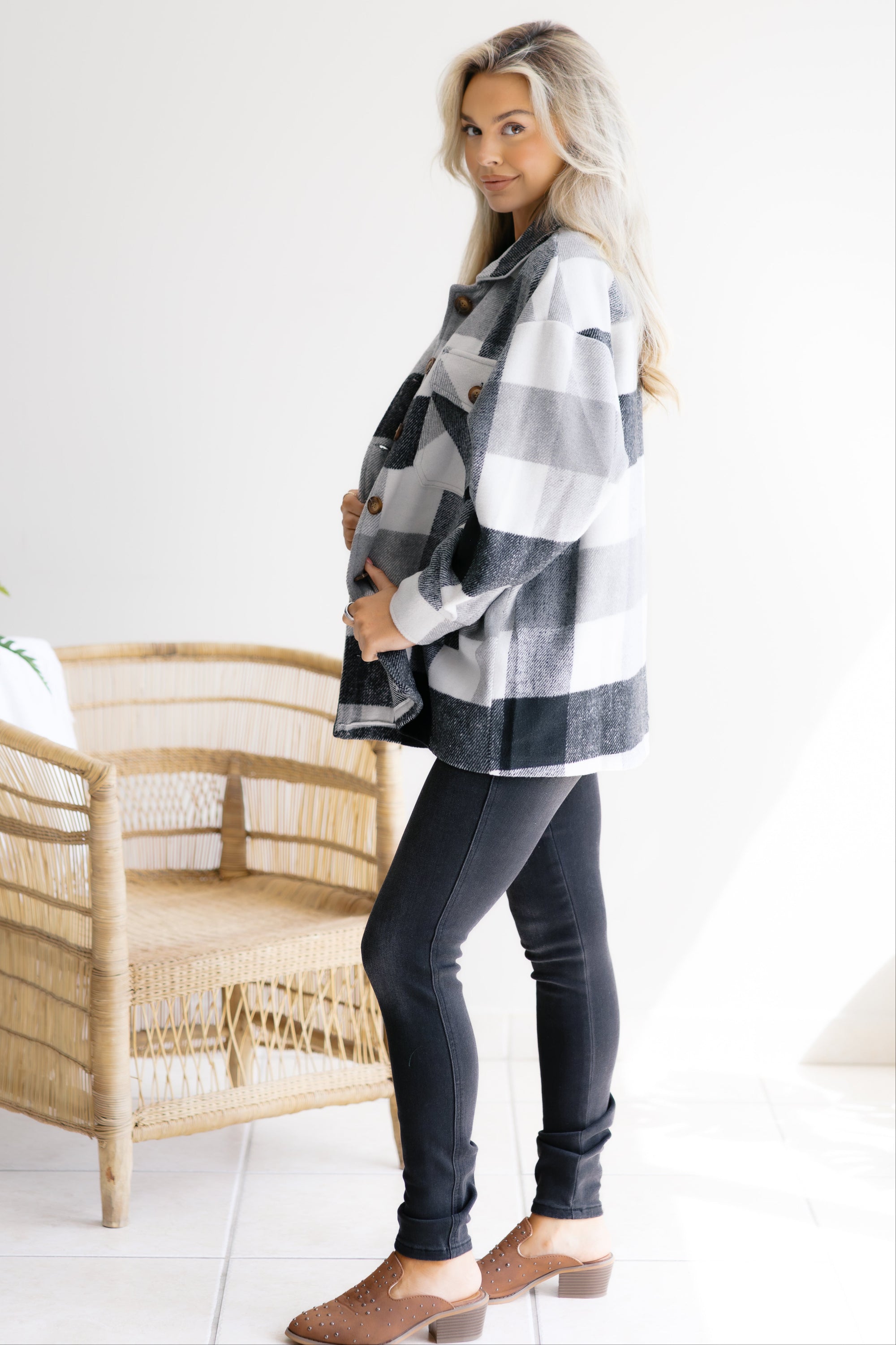 Woman wearing a plaid shirt and dark jeans standing in a room with a wicker chair.