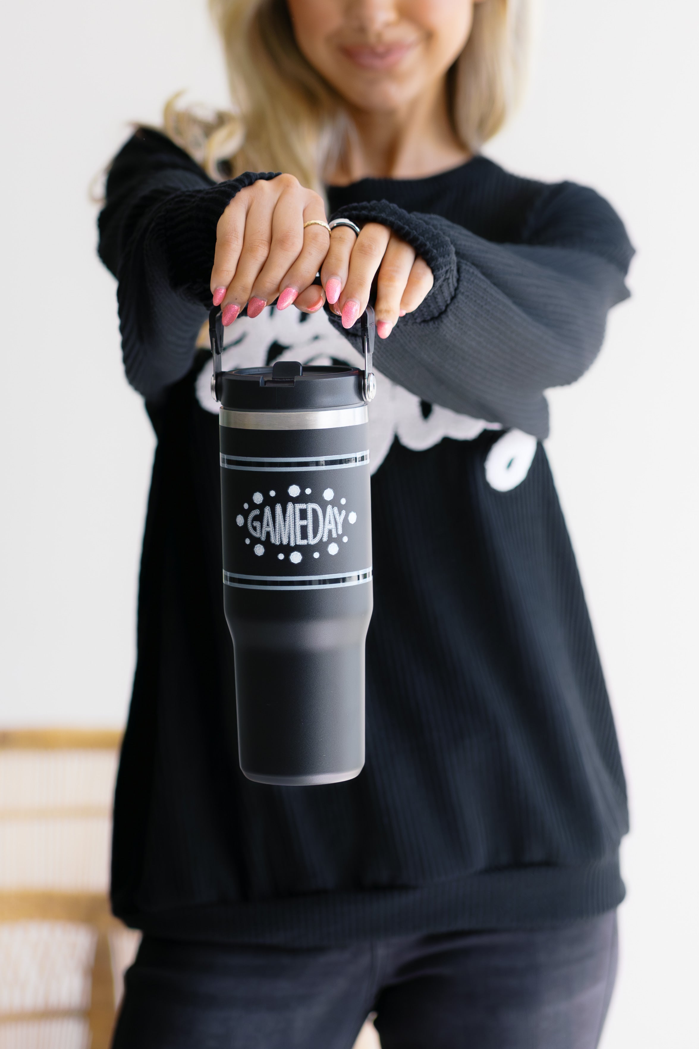 Person holding a black tumbler with 'GAMEDAY' text against a neutral background