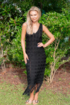 Woman wearing a black dress with fringe standing outdoors among greenery