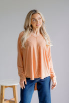 Woman wearing a peach long-sleeve top and blue jeans against a plain background