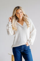 Woman wearing a soft white sweater and blue jeans against a plain background