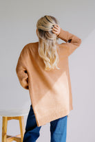Person wearing a tan sweater and blue jeans with a plain background