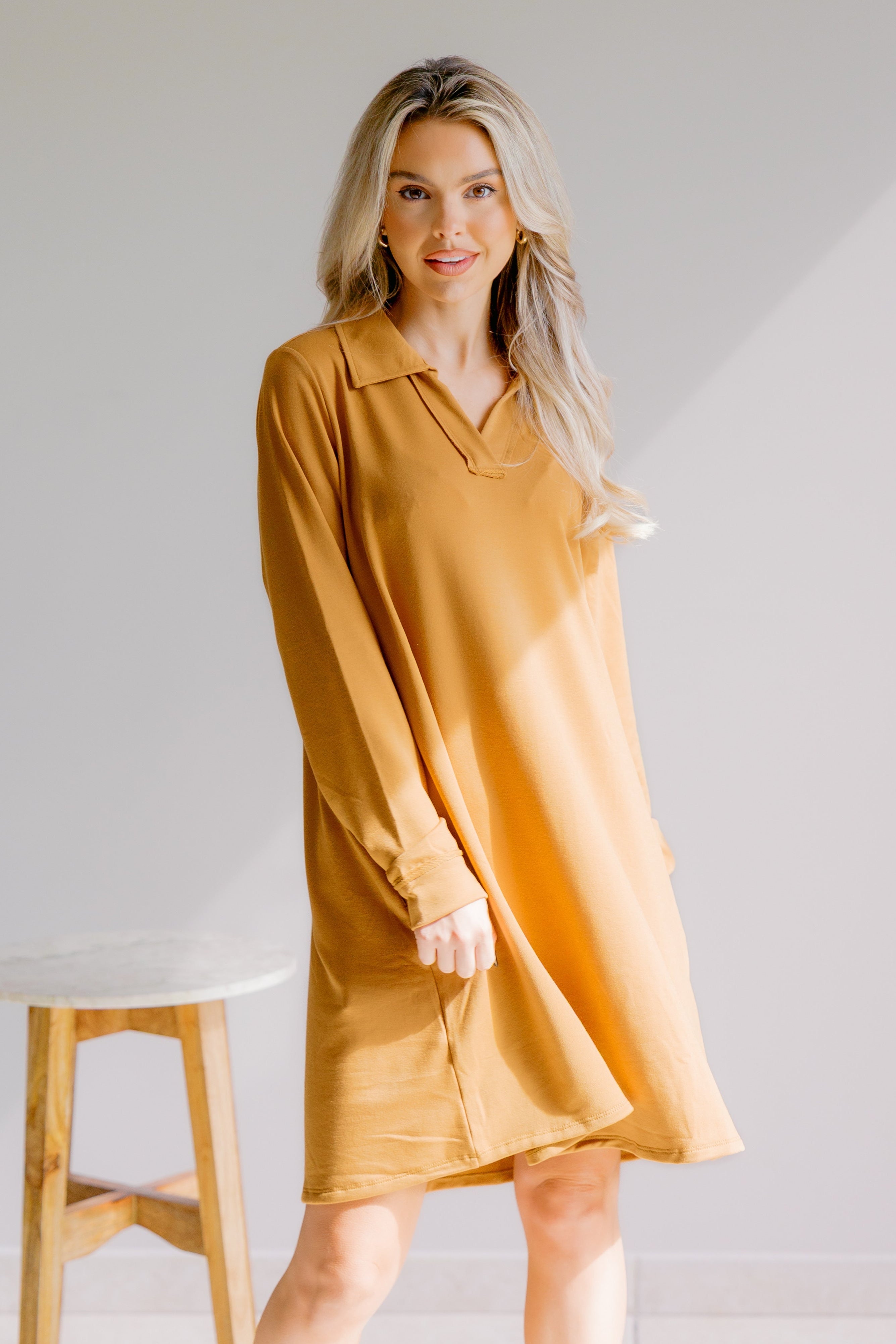 Woman wearing a mustard yellow dress standing against a plain background