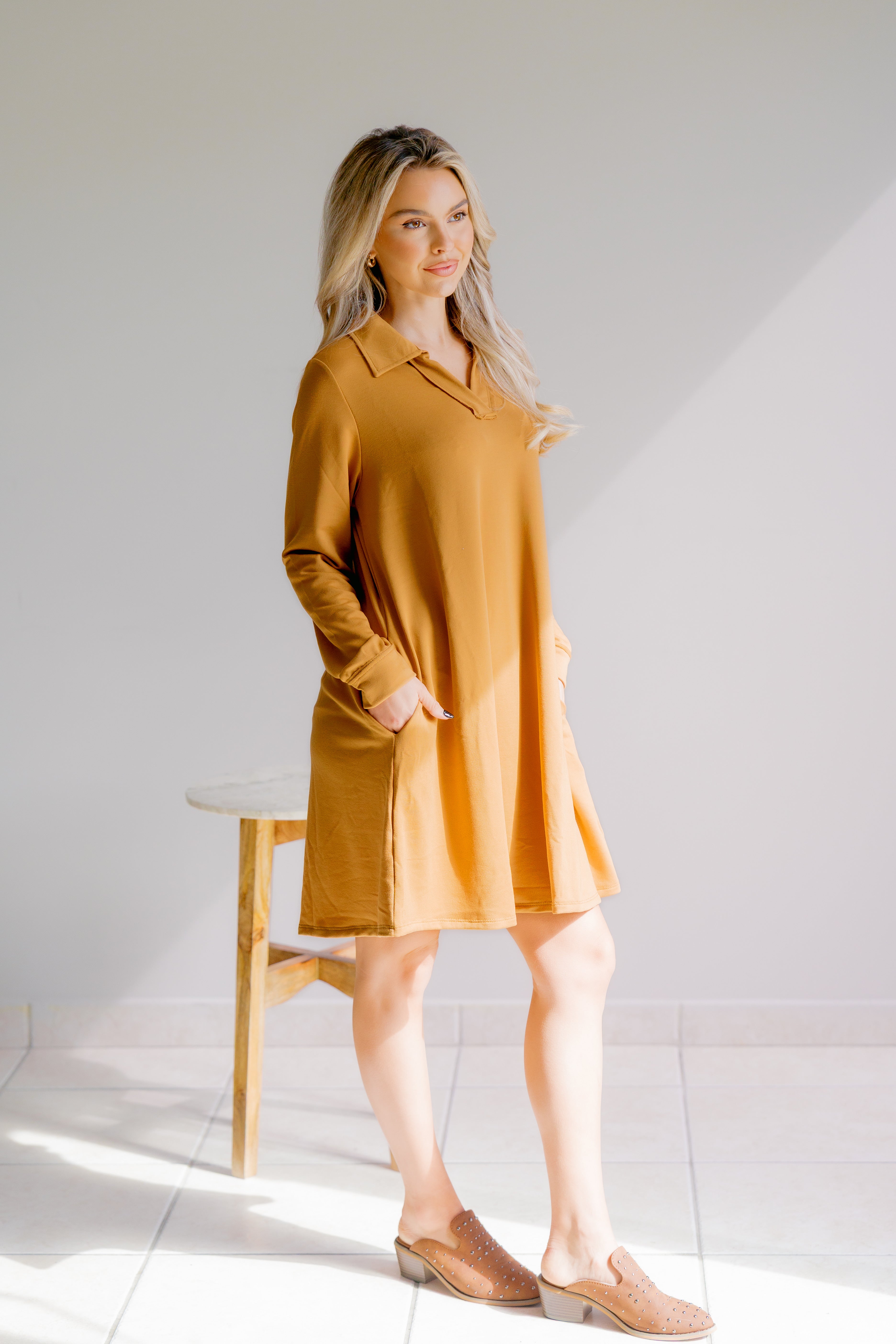 Woman wearing a mustard yellow dress standing against a white background