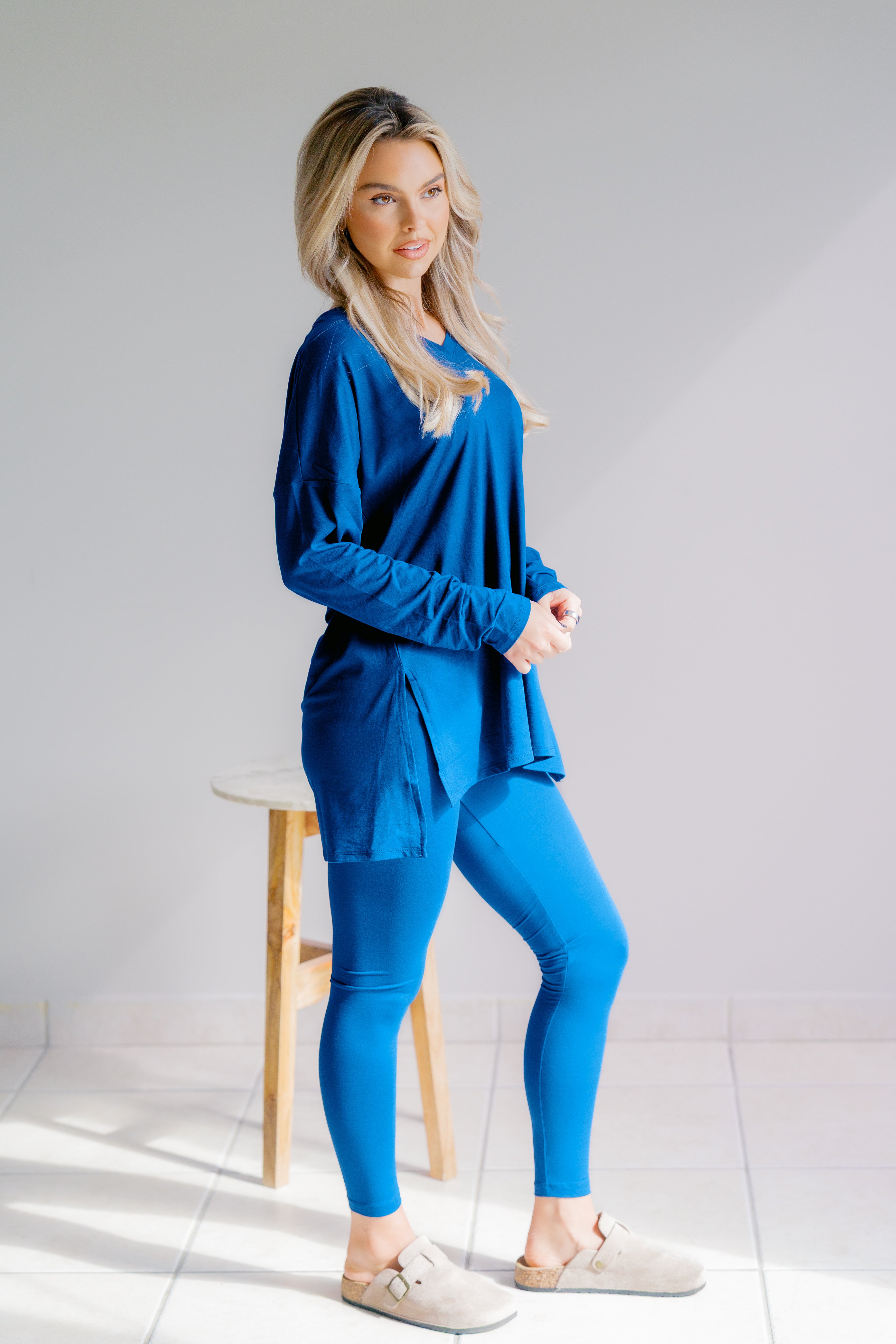 Woman wearing a blue outfit sitting on a stool against a white background