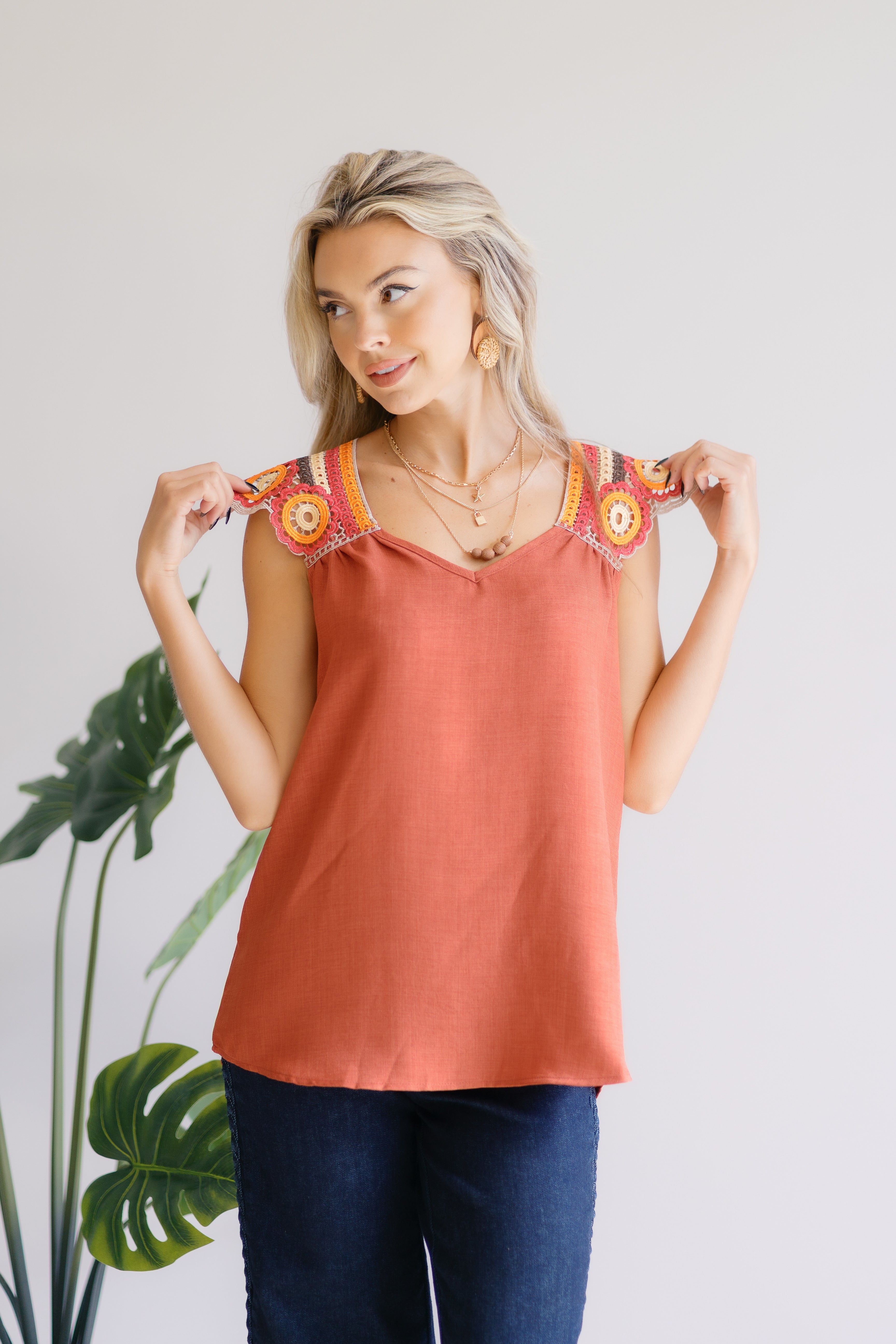 Woman wearing a rust-colored sleeveless top with colorful embroidery, standing against a white background.