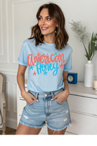 Woman wearing a light blue t-shirt with 'American Honey' text in a home setting