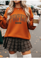 Person wearing an orange 'Pumpkin Season' sweatshirt and plaid skirt, holding a coffee cup.