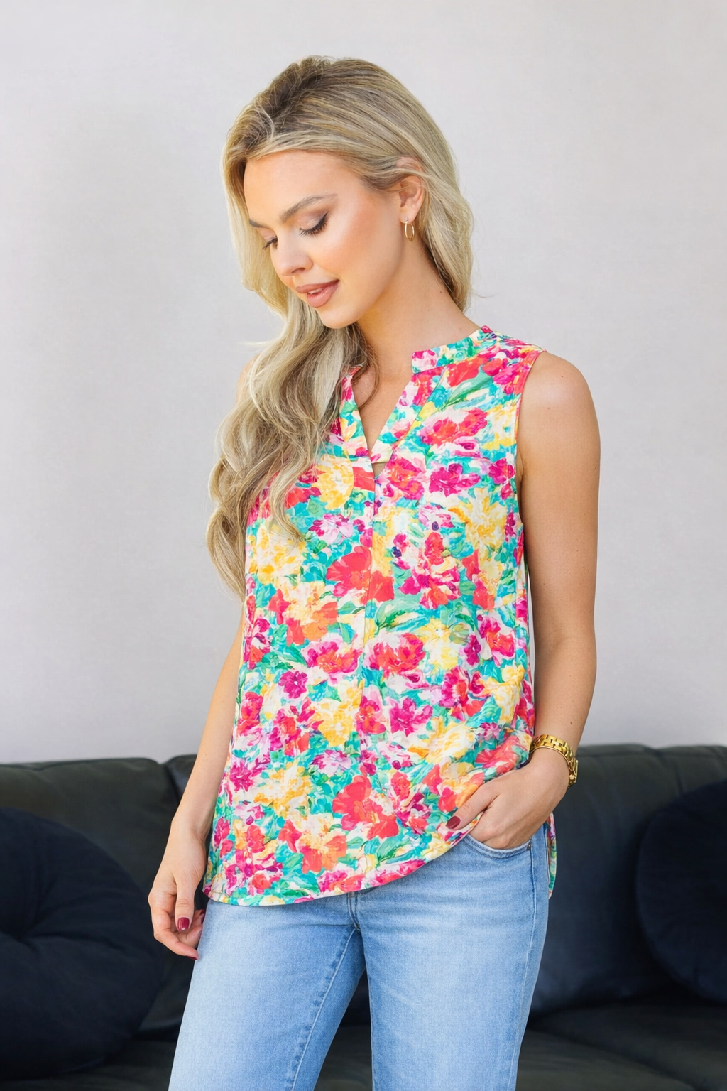 Woman wearing a colorful floral sleeveless top and blue jeans against a gray background.